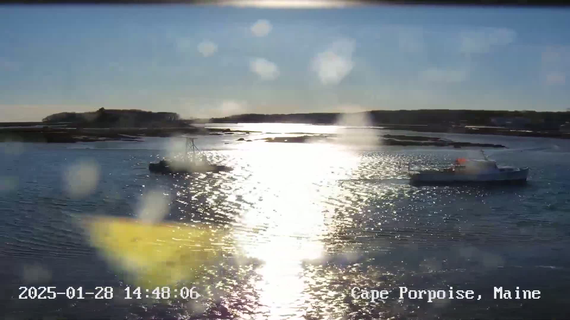 Two boats are on a calm, sunlit body of water near a shoreline with low-lying land.