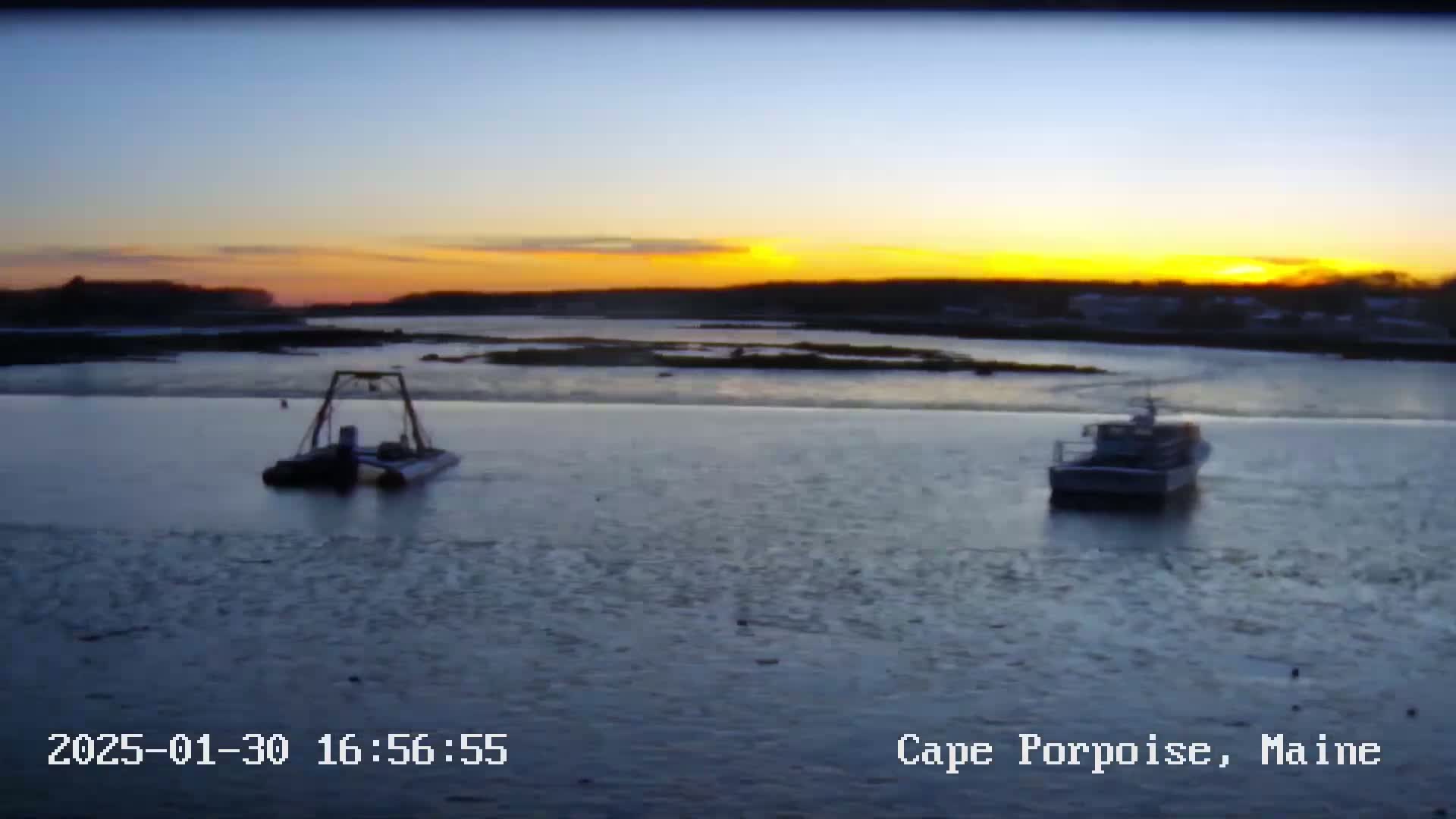 Two boats are moored on partially frozen water at sunset.