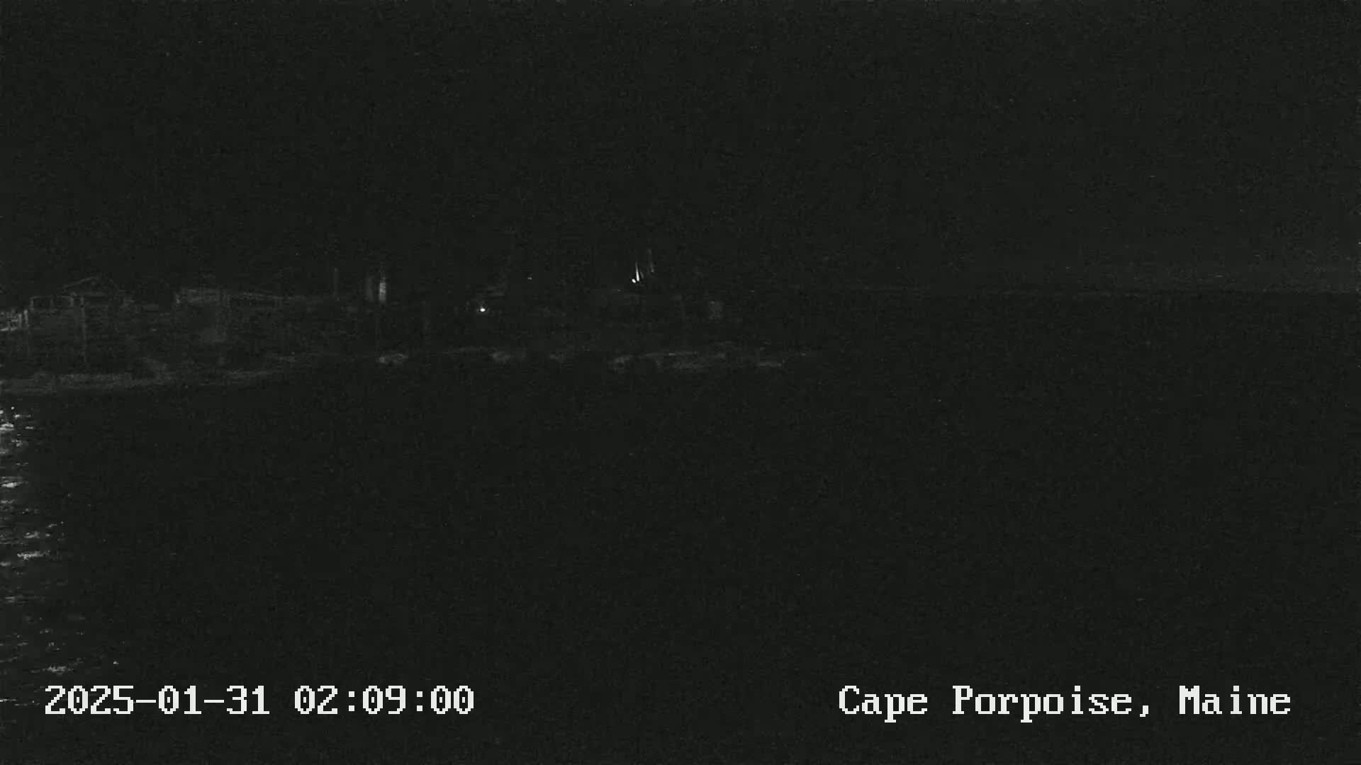 A dark, nighttime image shows a shoreline with a few faint lights in the distance, over dark water.