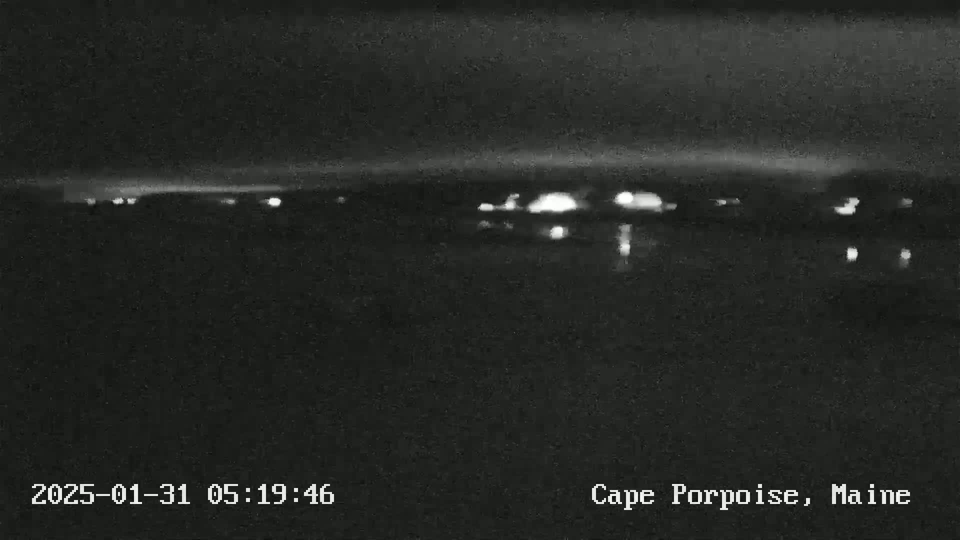 A nighttime, low-light view of a dark body of water reflecting faint lights from a distant shoreline.
