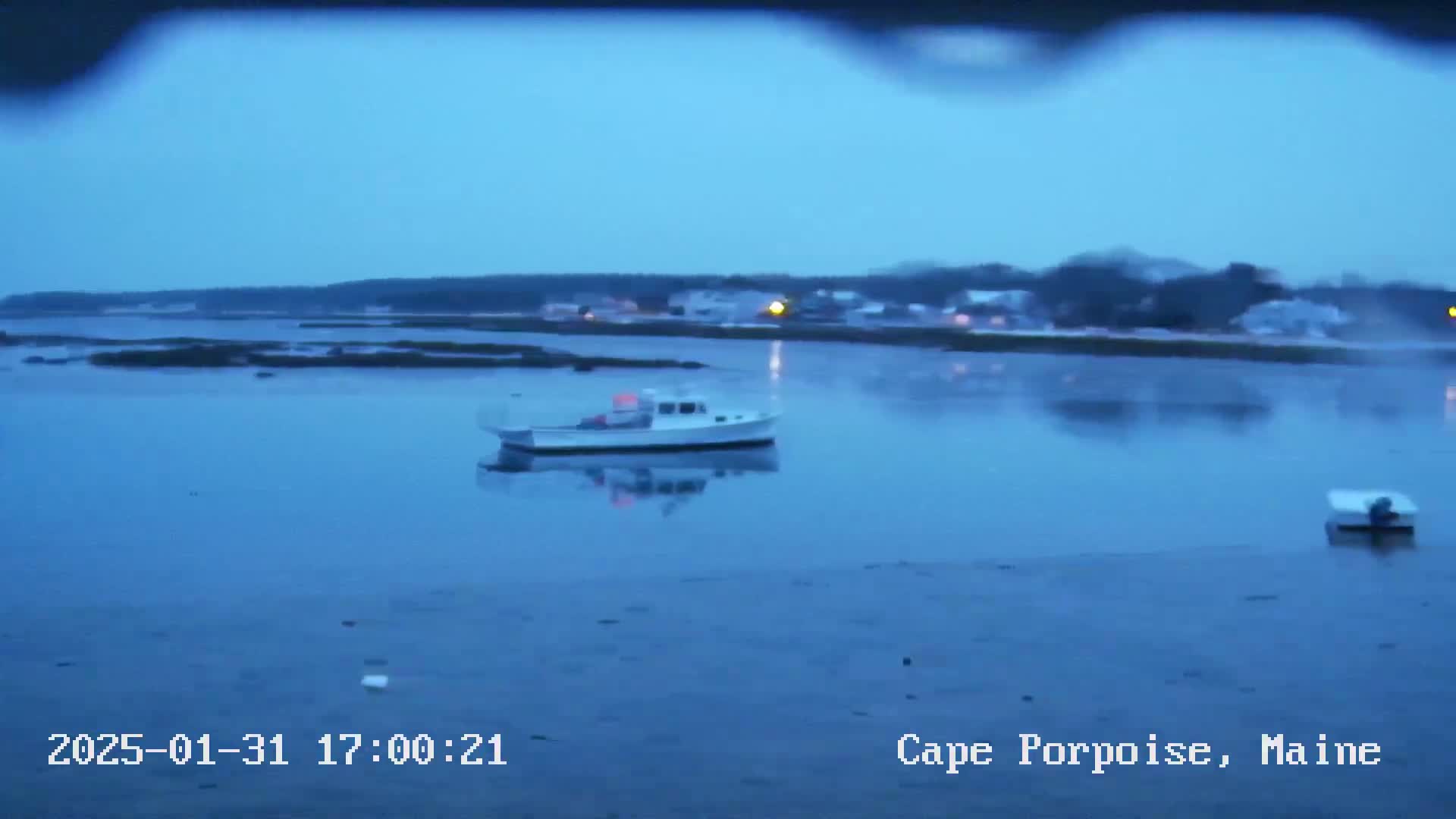 A small white boat is moored in calm, blue water under an overcast sky, with a distant shoreline visible.