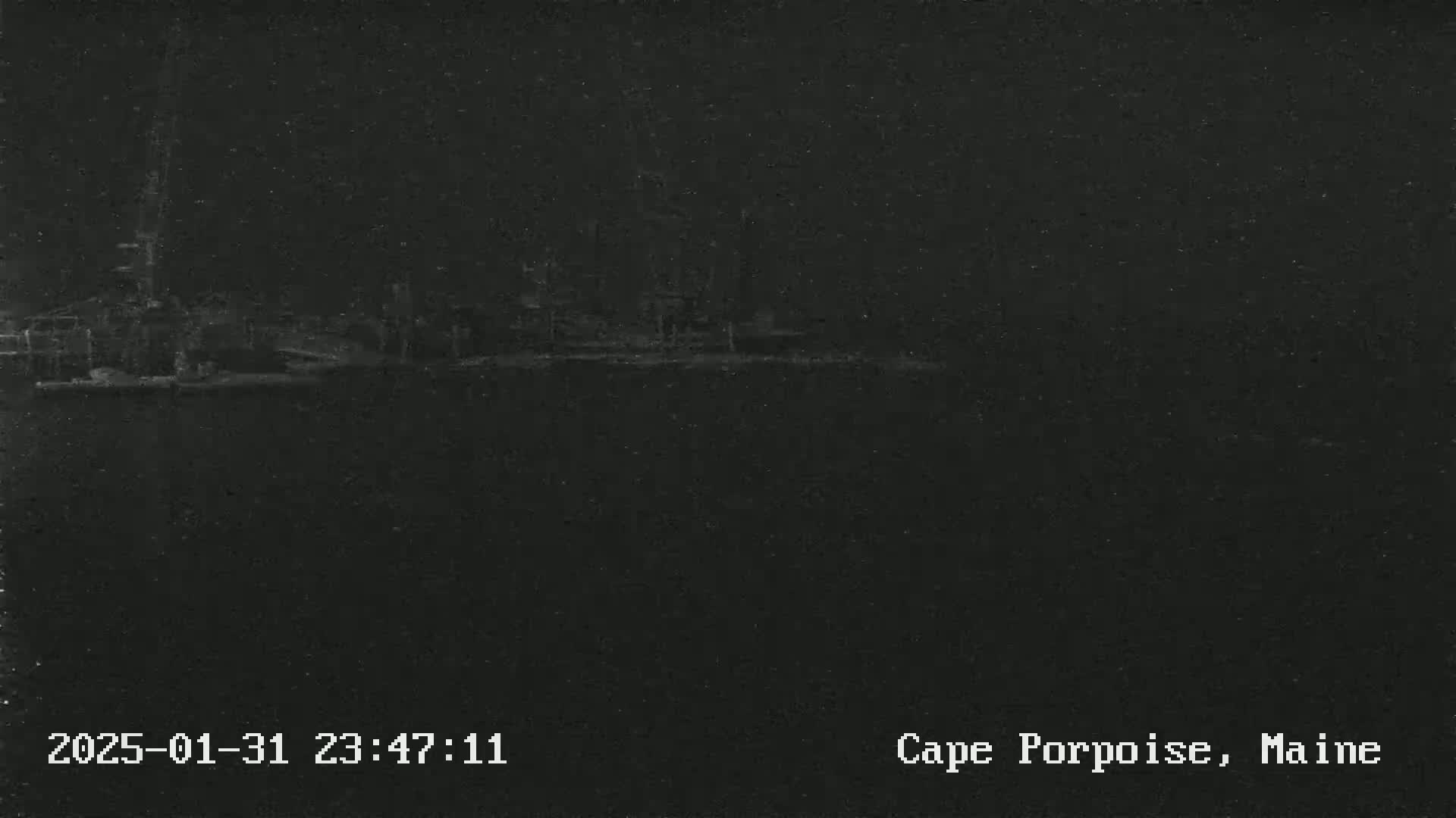 A dark, nighttime image shows a blurry, indistinct shoreline under a dark sky.