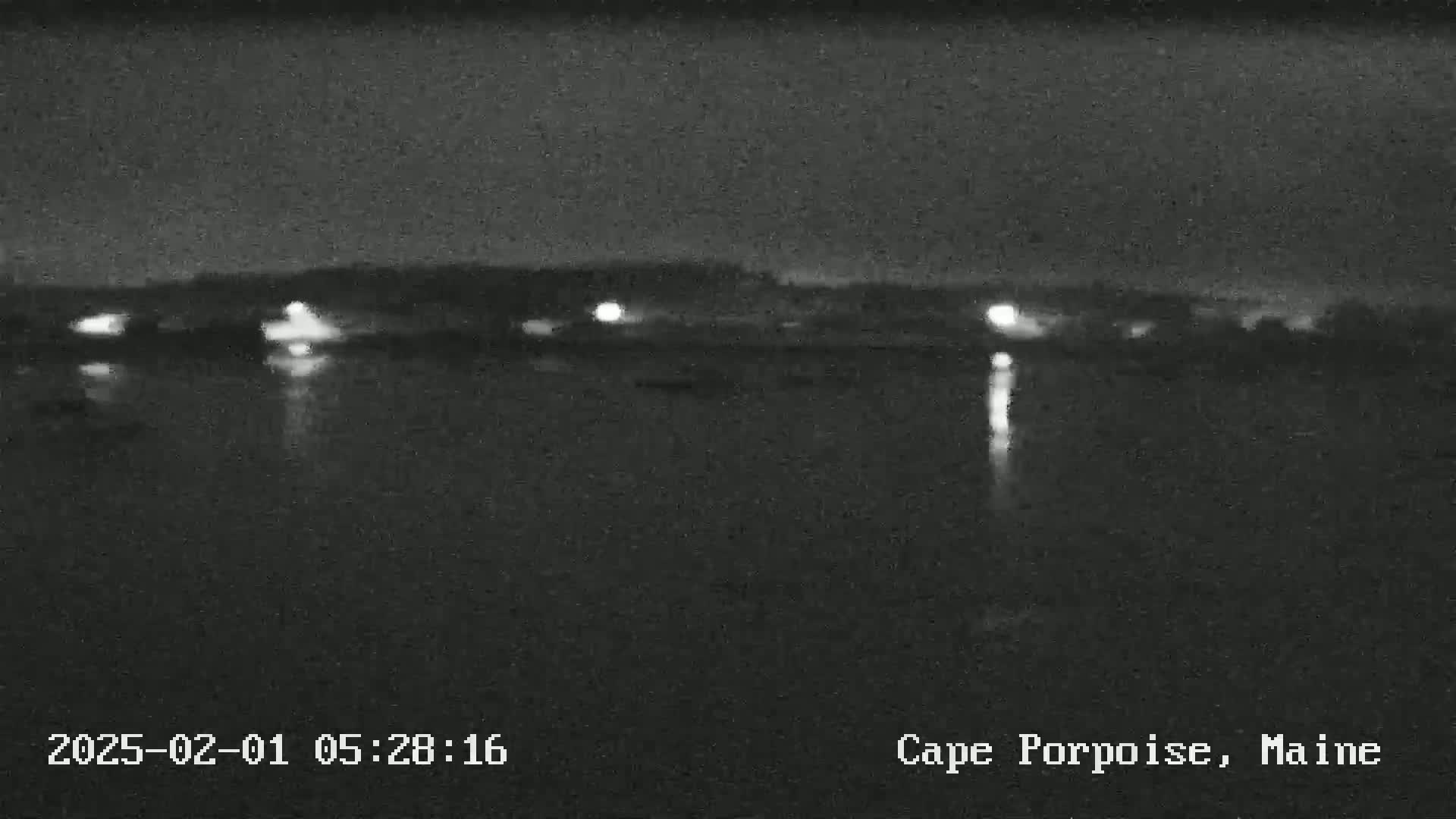 A nighttime, low-light view of a body of water reflecting scattered lights from a distant shoreline.