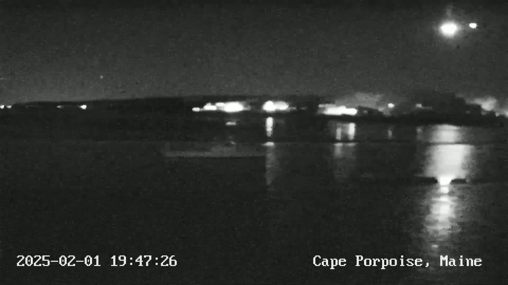A nighttime, blurry view of a body of water reflecting distant lights under a bright moon.