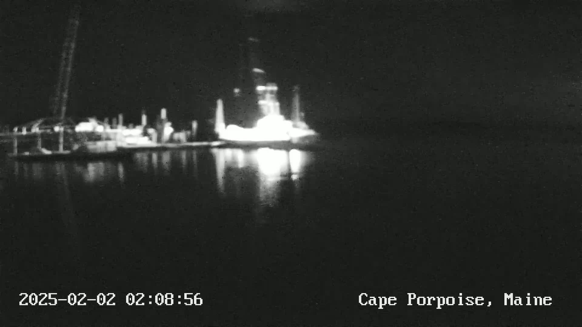 A nighttime, blurry view shows a brightly lit structure on the water's edge, reflecting in the dark water.