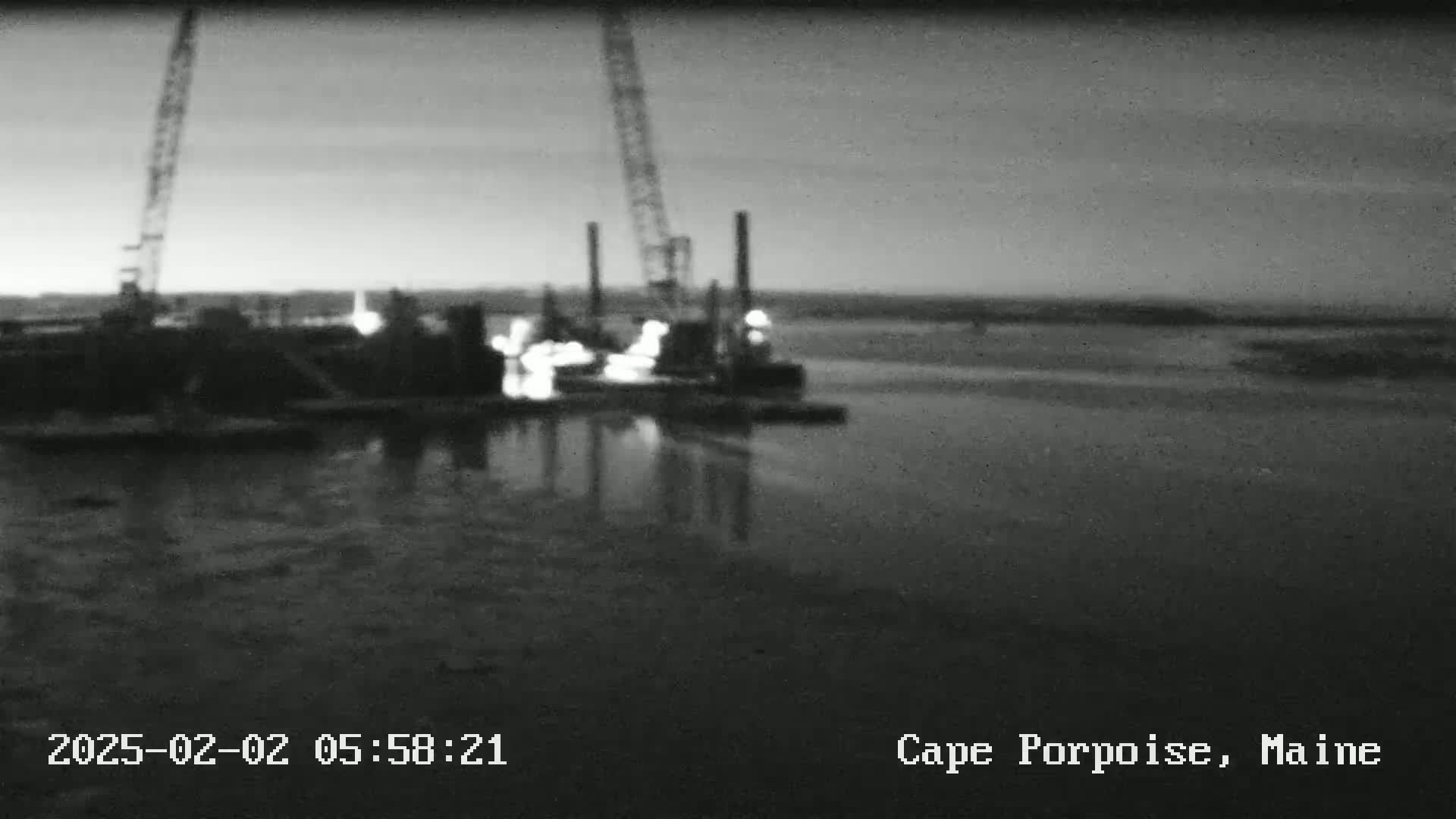 A nighttime, low-light view of construction equipment and structures on a body of water.