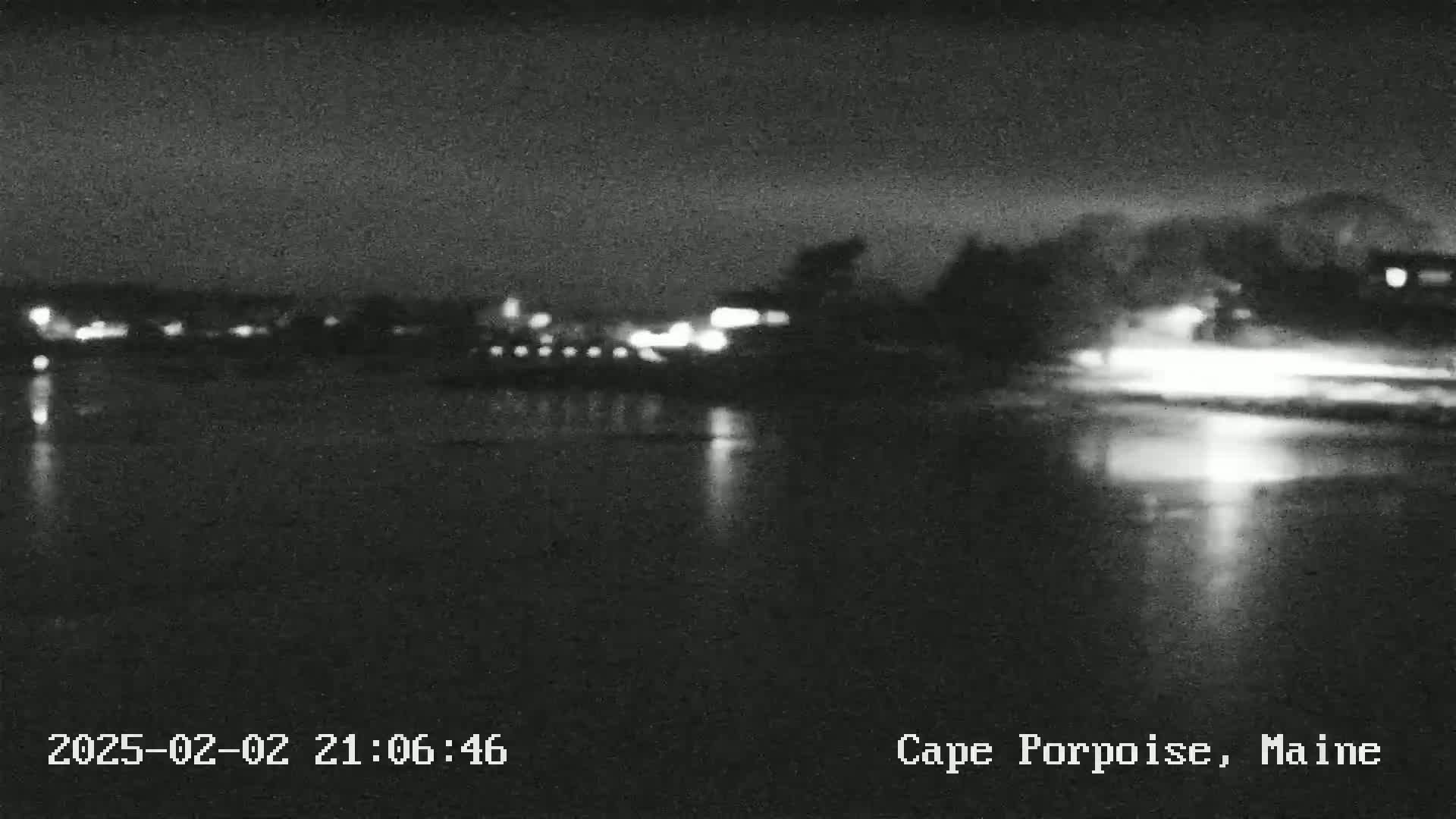 A nighttime, blurry view of a calm body of water reflecting distant lights from a town under a dark sky.