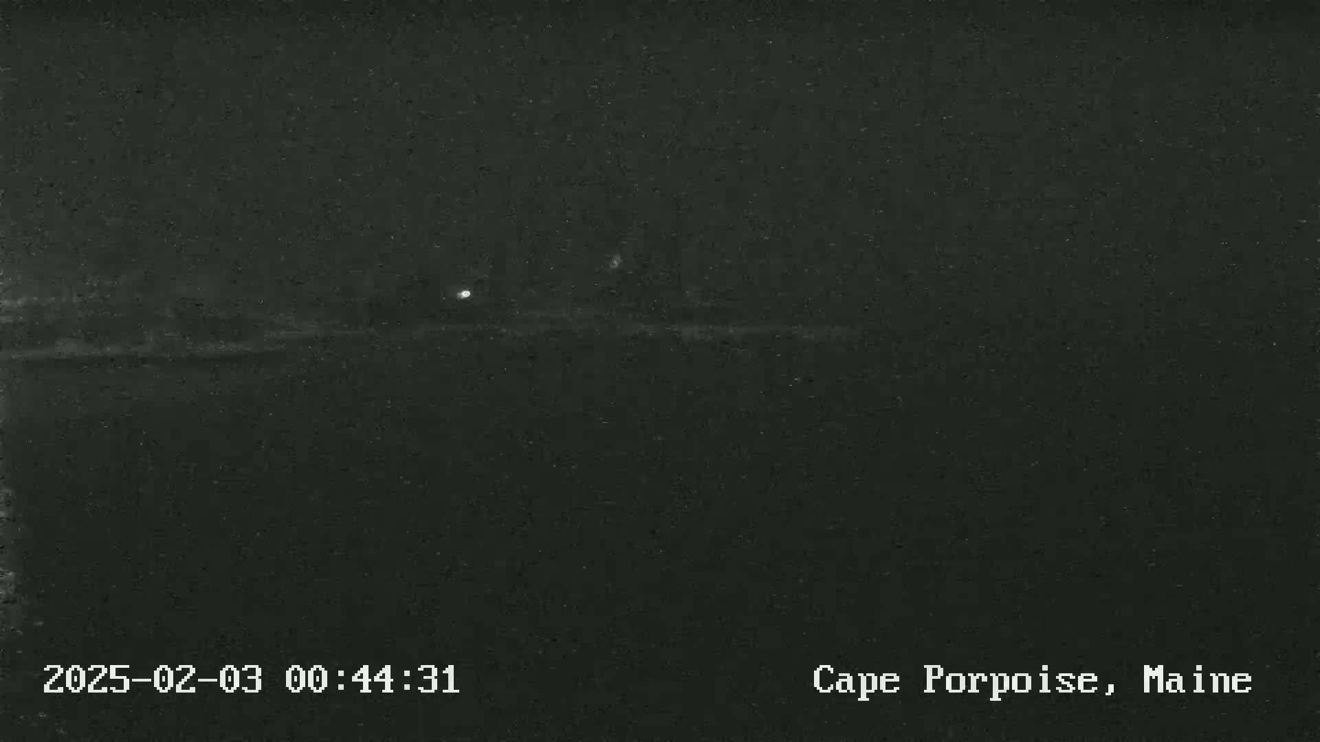 A nighttime, low-light image shows a dark, flat landscape with a single, faint light source in the distance.