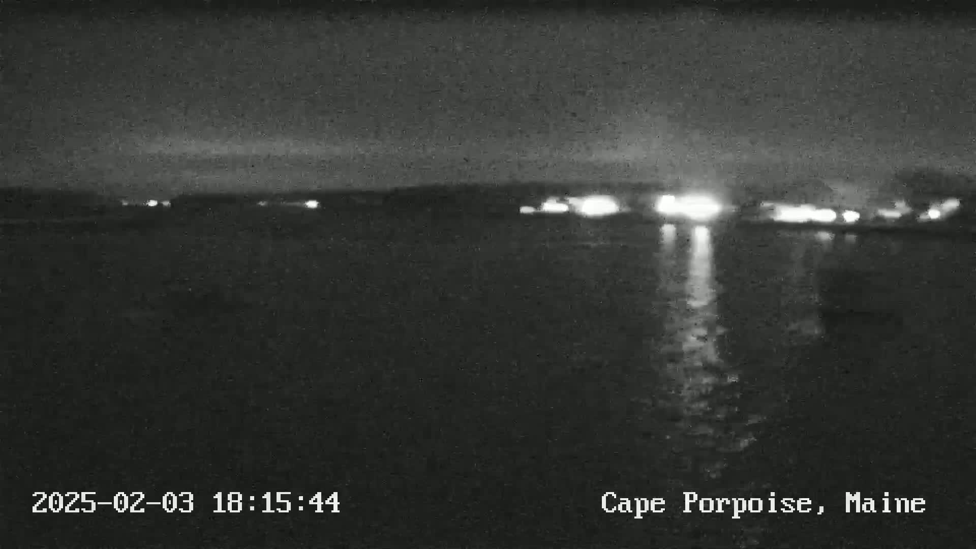 A nighttime view of a dark body of water reflecting distant lights under a mostly clear sky.