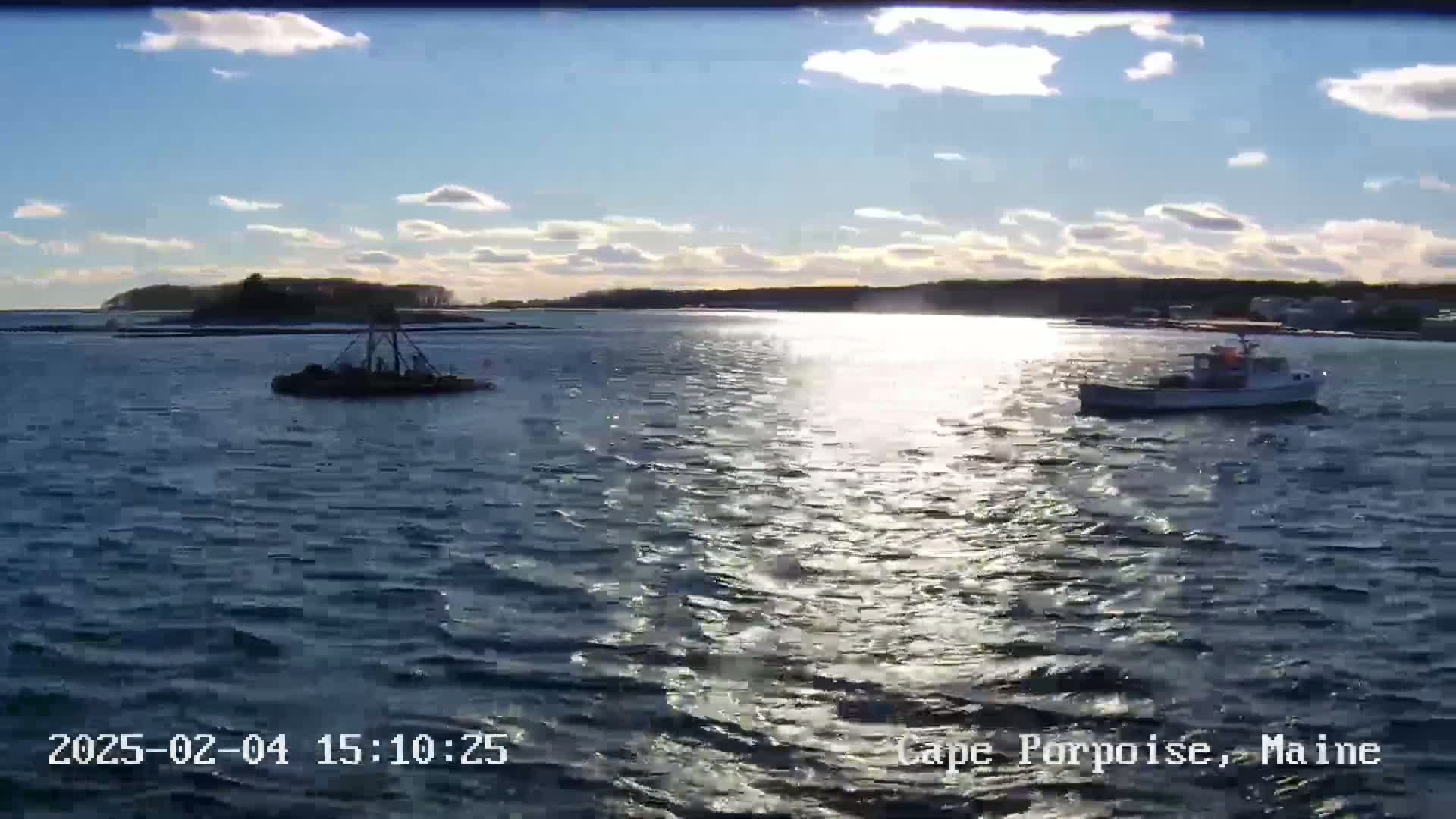 Two boats are on a partly sunny body of water with a distant shoreline under a partly cloudy sky.