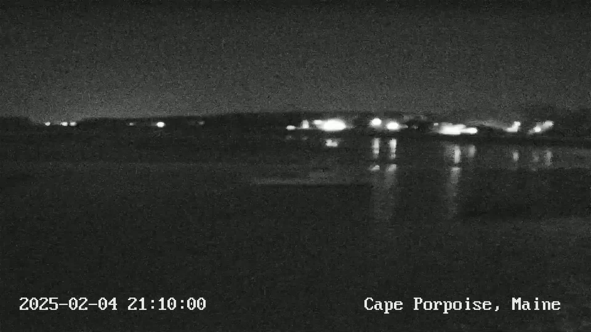 A nighttime view of a dark body of water reflecting distant lights across a shoreline.