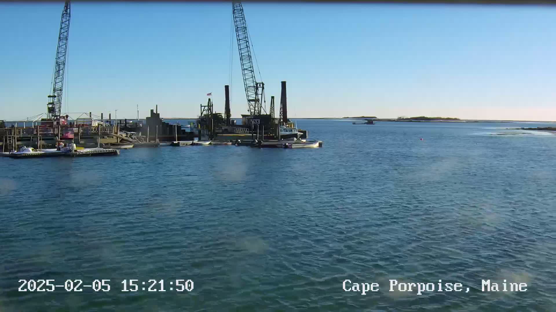 A large crane and several boats are moored in a calm harbor on a clear, sunny day.