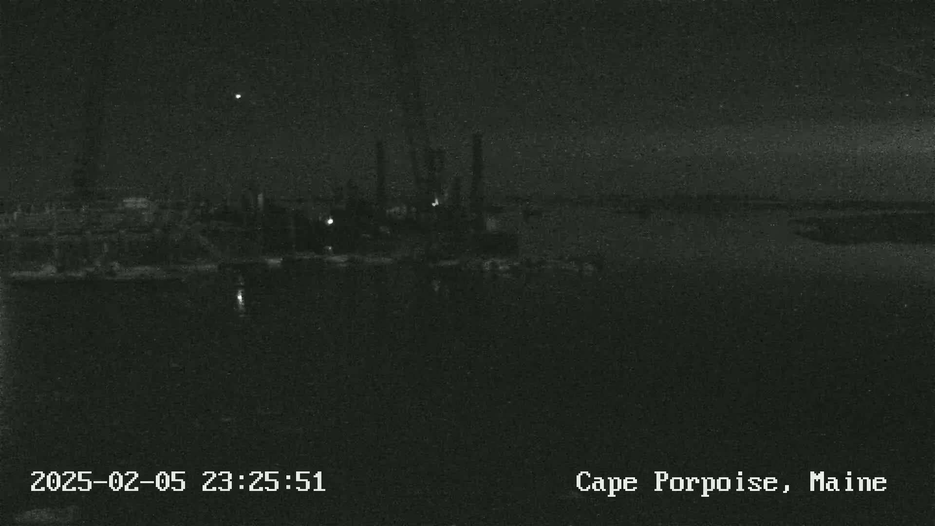 A nighttime, low-light view of a dark harbor with a few faint lights and some structures visible in the distance.