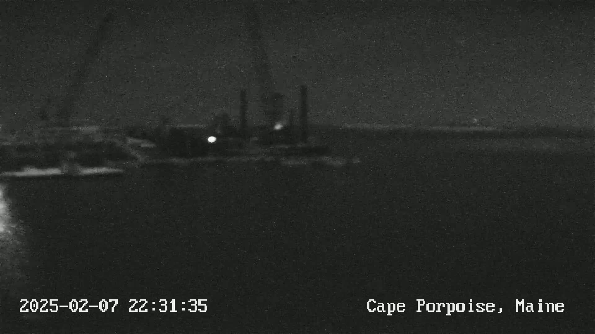 A nighttime, blurry view of a dark body of water with faintly visible structures and lights in the distance under a dark sky.