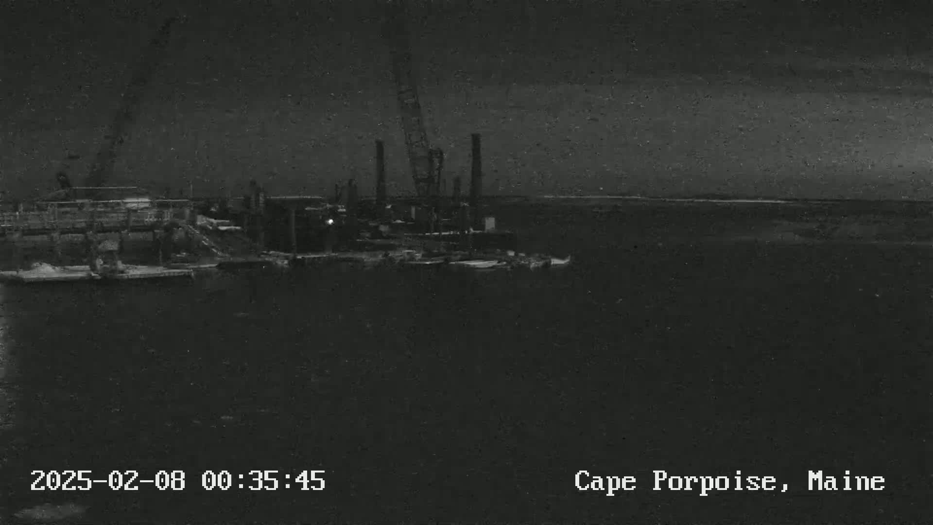 A nighttime, low-light image shows a dark body of water with construction equipment and structures on a dock.
