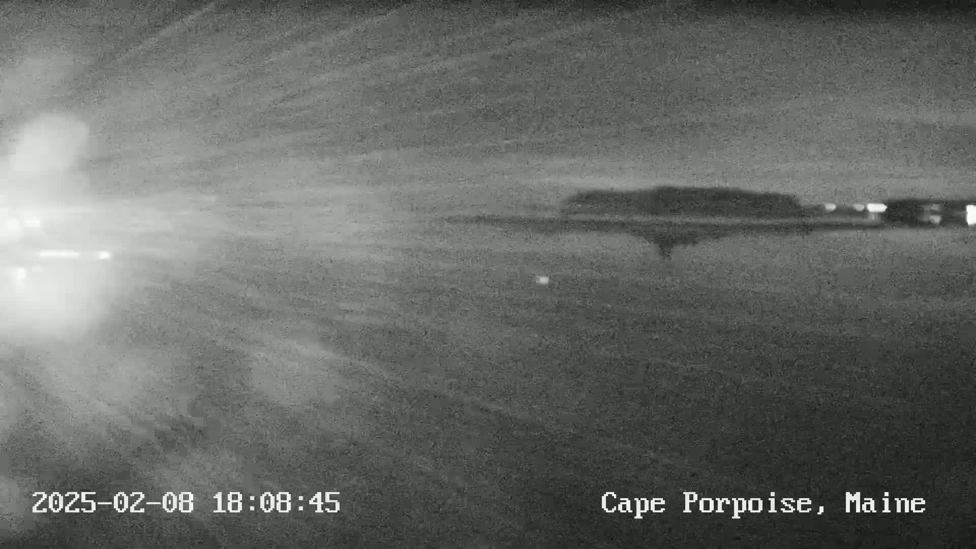 A nighttime, snowy scene shows a blurry, dark road leading toward a dimly lit landscape.