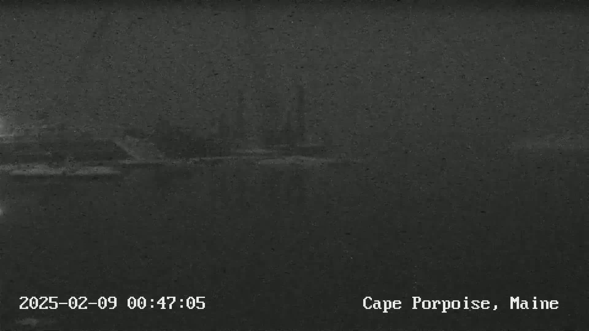 A dark, blurry nighttime image shows a body of water and indistinct land features under a cloudy sky.