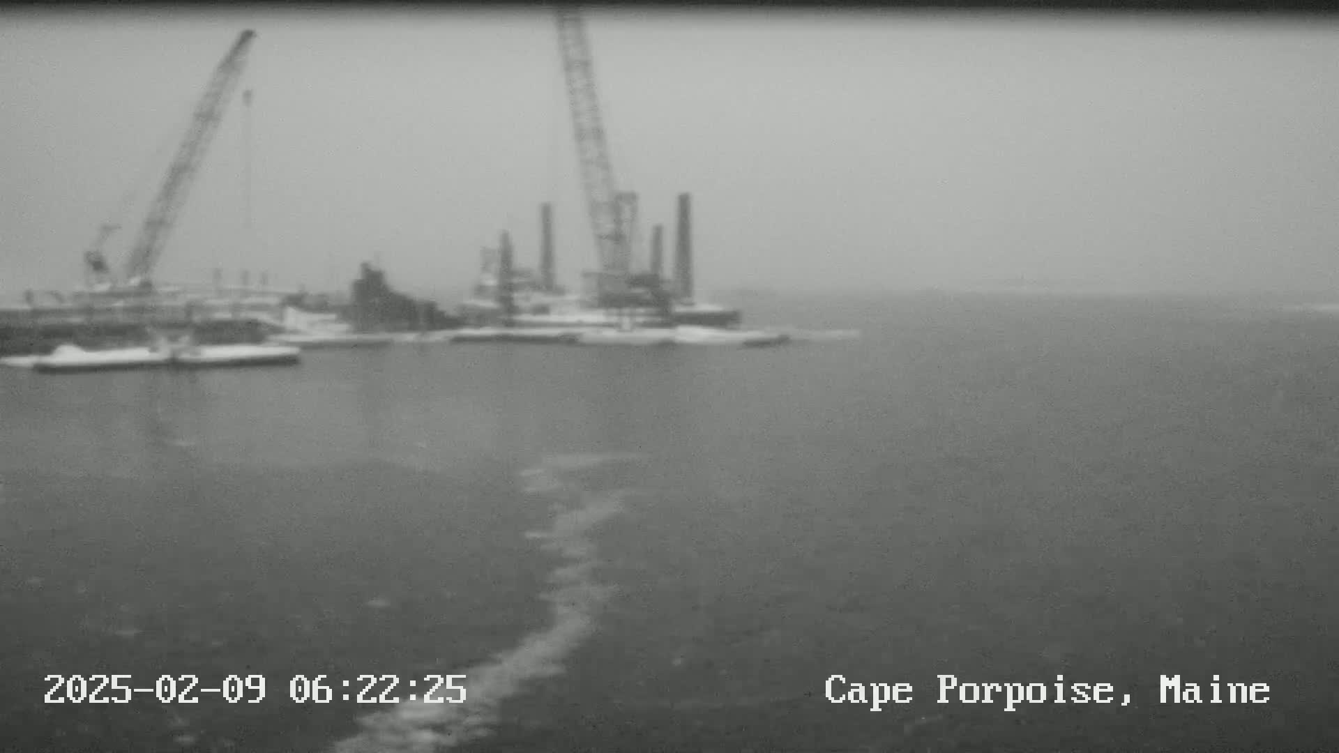 A snowy, hazy view shows industrial cranes and structures on a body of water.