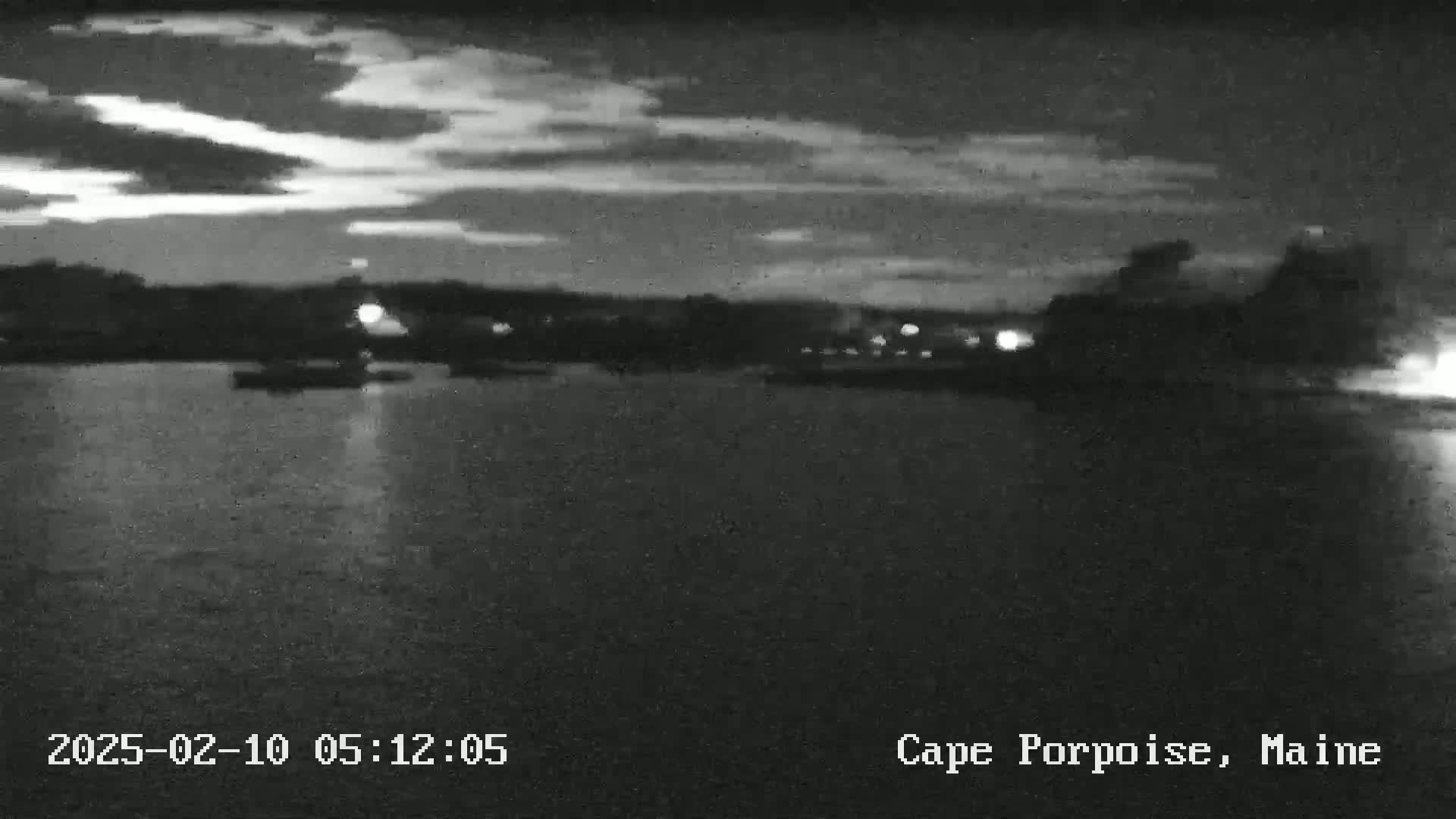 A nighttime, low-light view of a body of water with a distant shoreline under a cloudy sky.