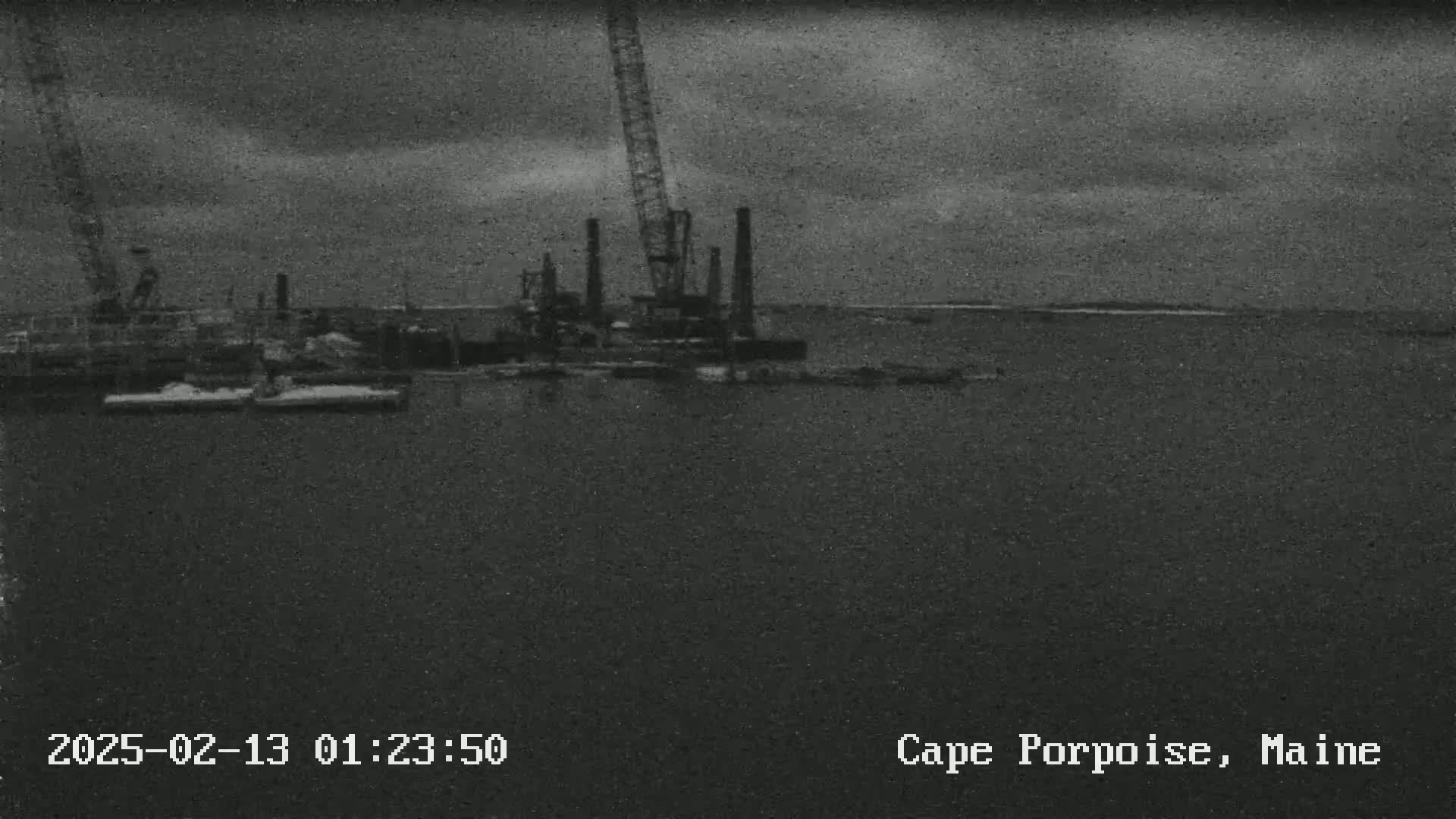 A large crane and other construction equipment are visible on the water under an overcast sky.