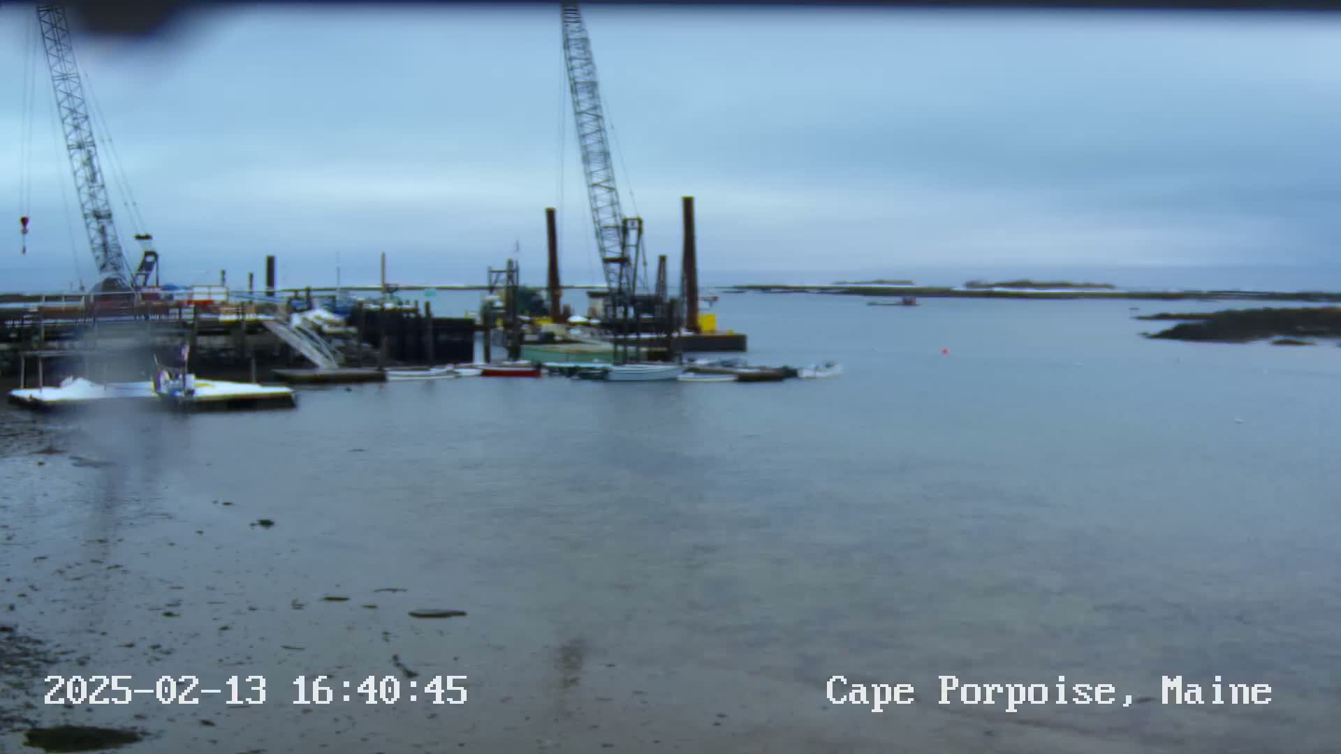 Several boats and construction cranes are situated at a dock in calm, overcast weather.
