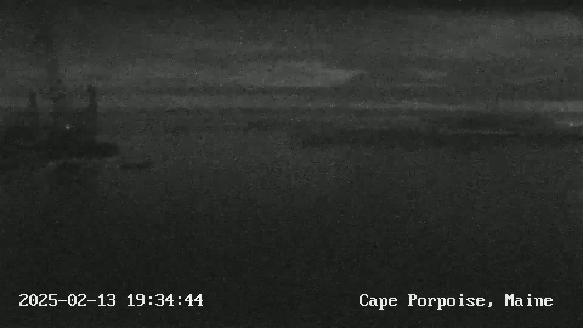 A dark, nighttime view of a dimly lit coastal area under a cloudy sky.