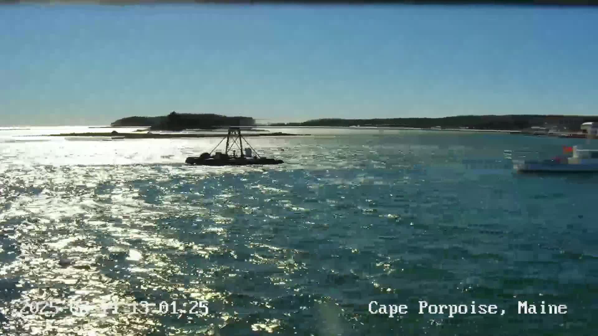 A body of water with a small boat and a larger vessel is visible under a sunny sky.