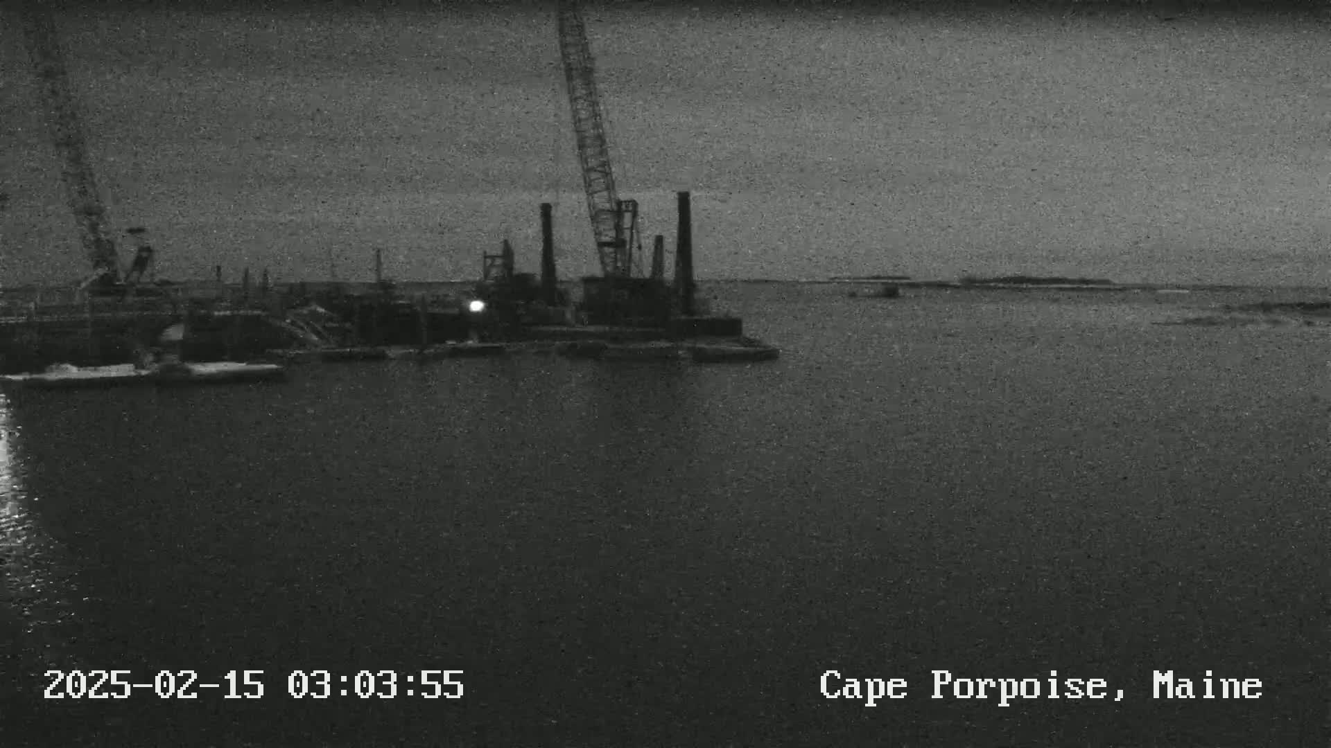 A construction site with cranes and structures is visible on a dark, possibly nighttime, body of water.