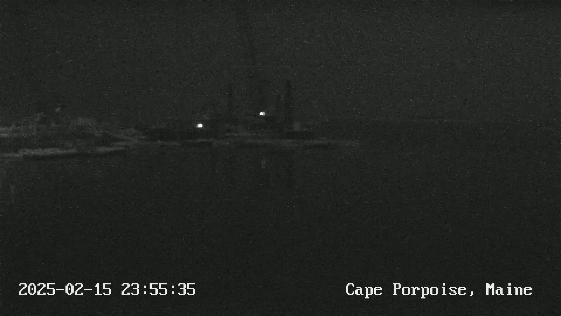 A nighttime, low-light view of a dark body of water with dimly lit structures visible in the distance.