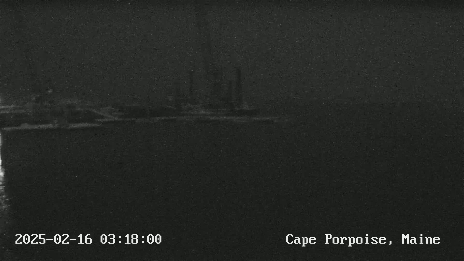 A dark, nighttime image shows a low-lying structure in the distance, possibly industrial, under a hazy or foggy sky.