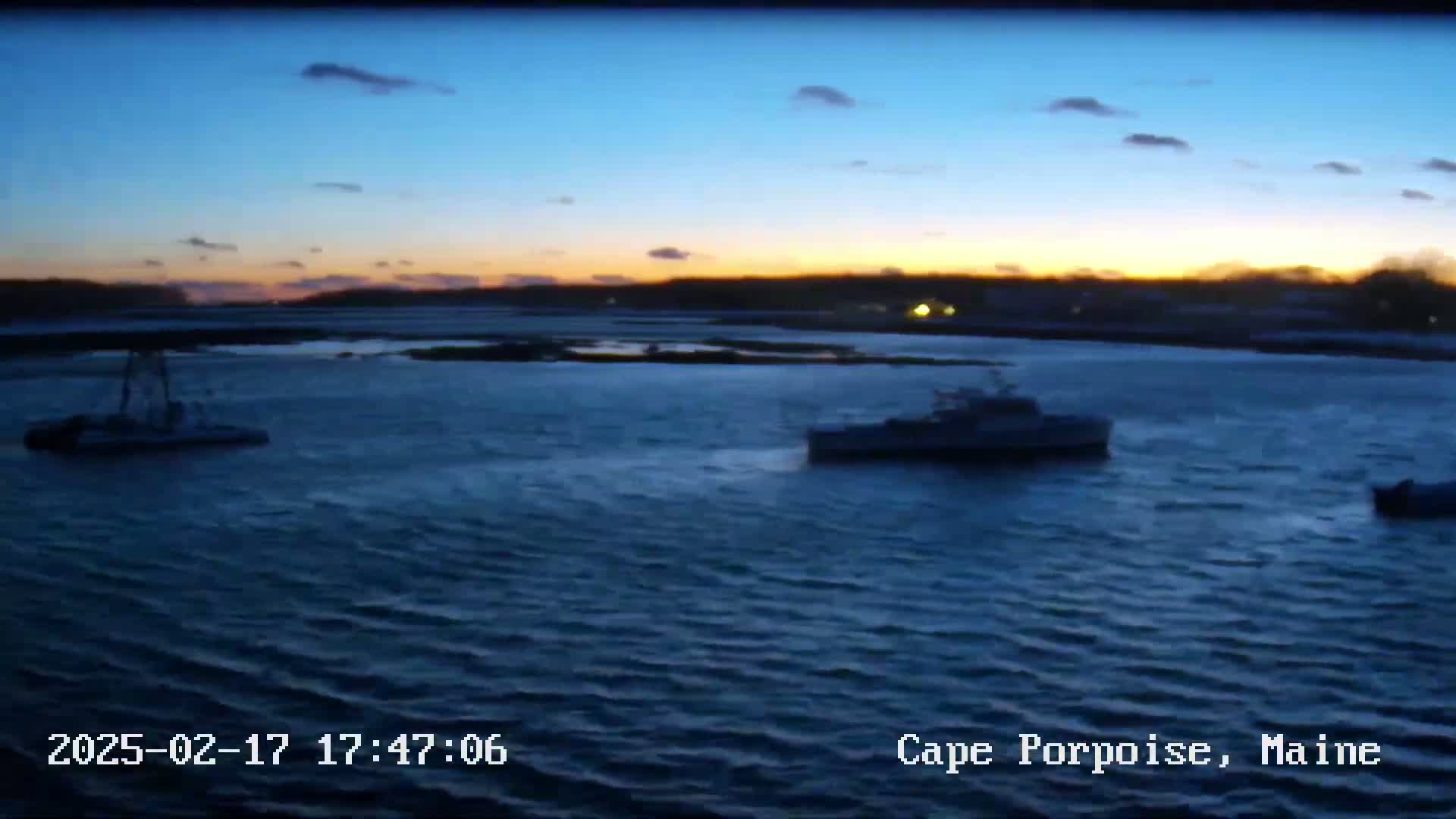 Three boats are on dark blue water at dusk under a mostly clear sky.