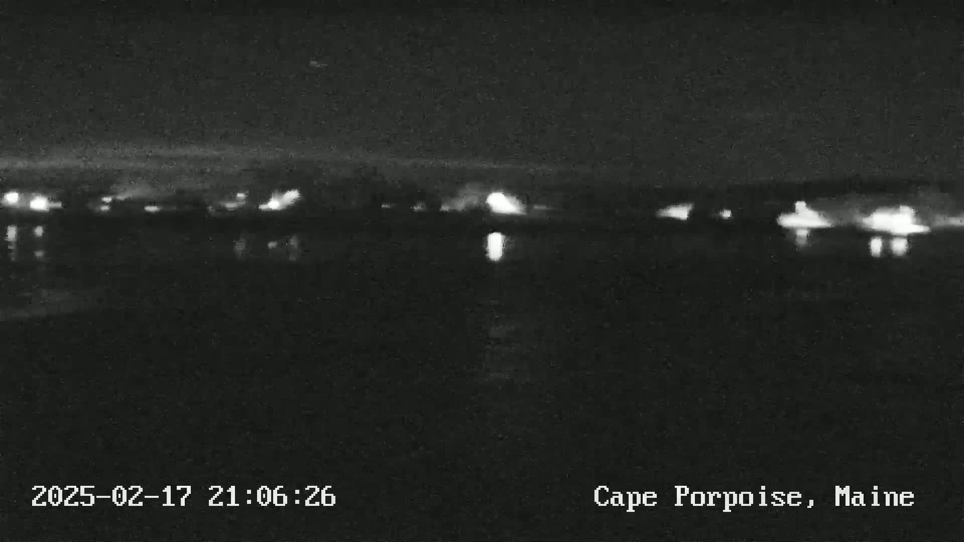 A nighttime, low-light view of a calm body of water reflecting the lights of a distant shoreline.