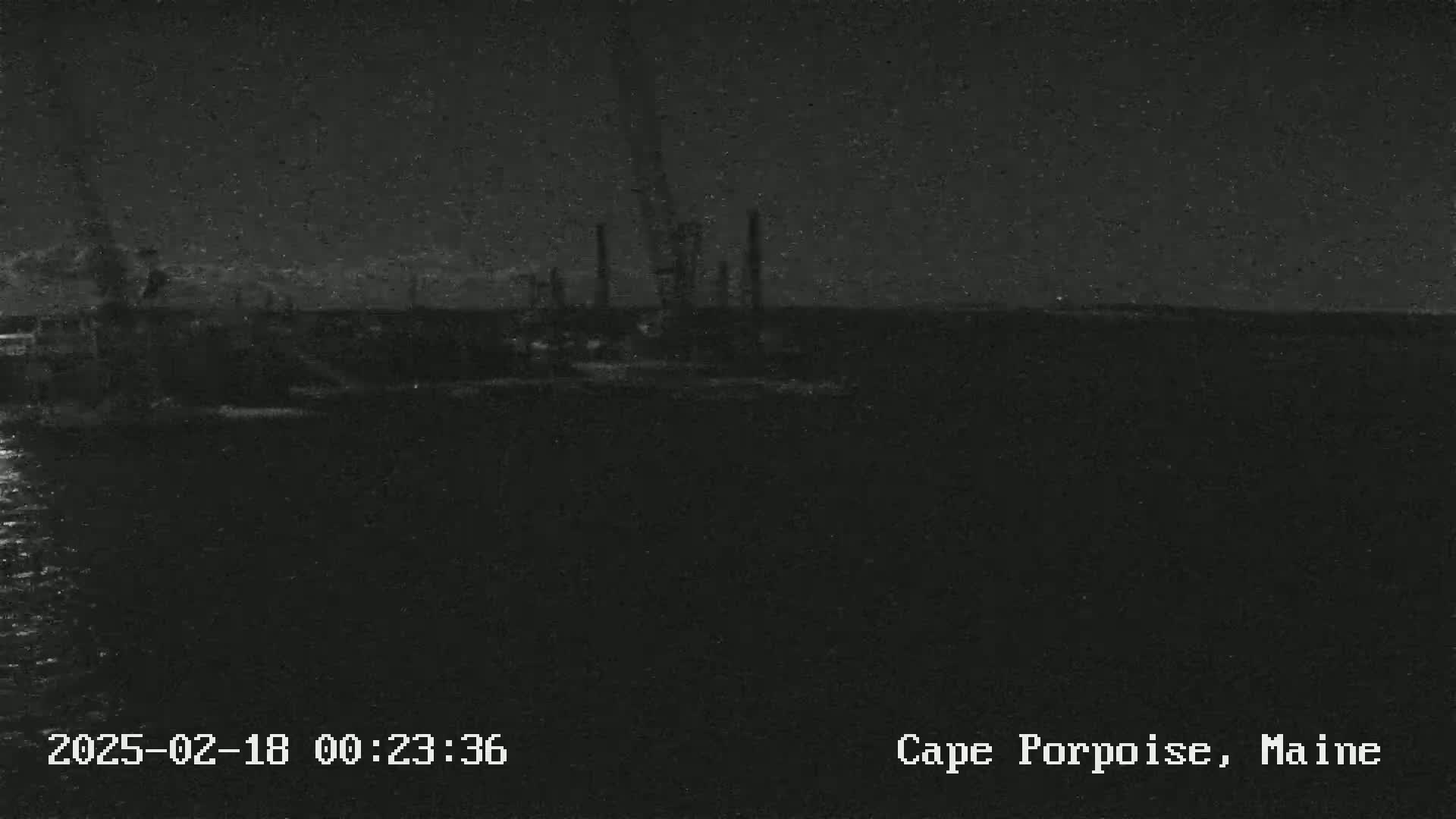 A nighttime, low-light view shows an industrial area near a body of water under a dark sky.