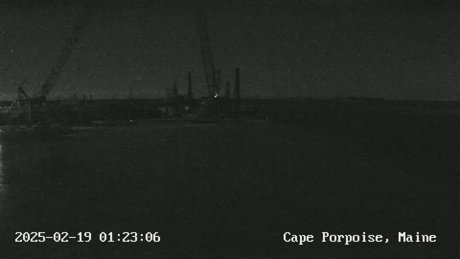 A nighttime, low-light image shows an industrial area with several tall structures silhouetted against a dark sky.