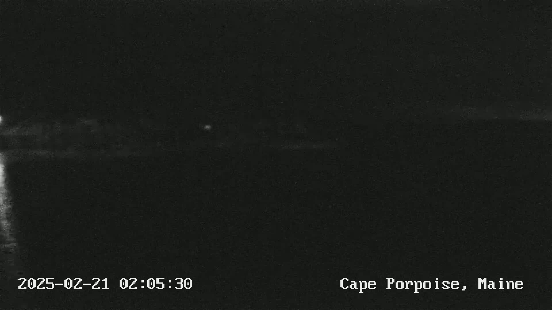 A nighttime, low-light image shows a dark horizon line with a faint, bright area possibly indicating distant lights.