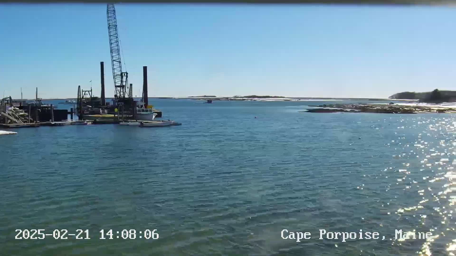 A large crane sits on a dock in a calm body of water under a clear blue sky.