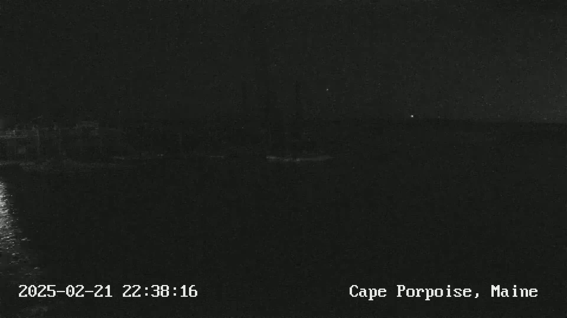 A dark, nighttime view of a body of water with a shoreline in the distance under a clear sky.