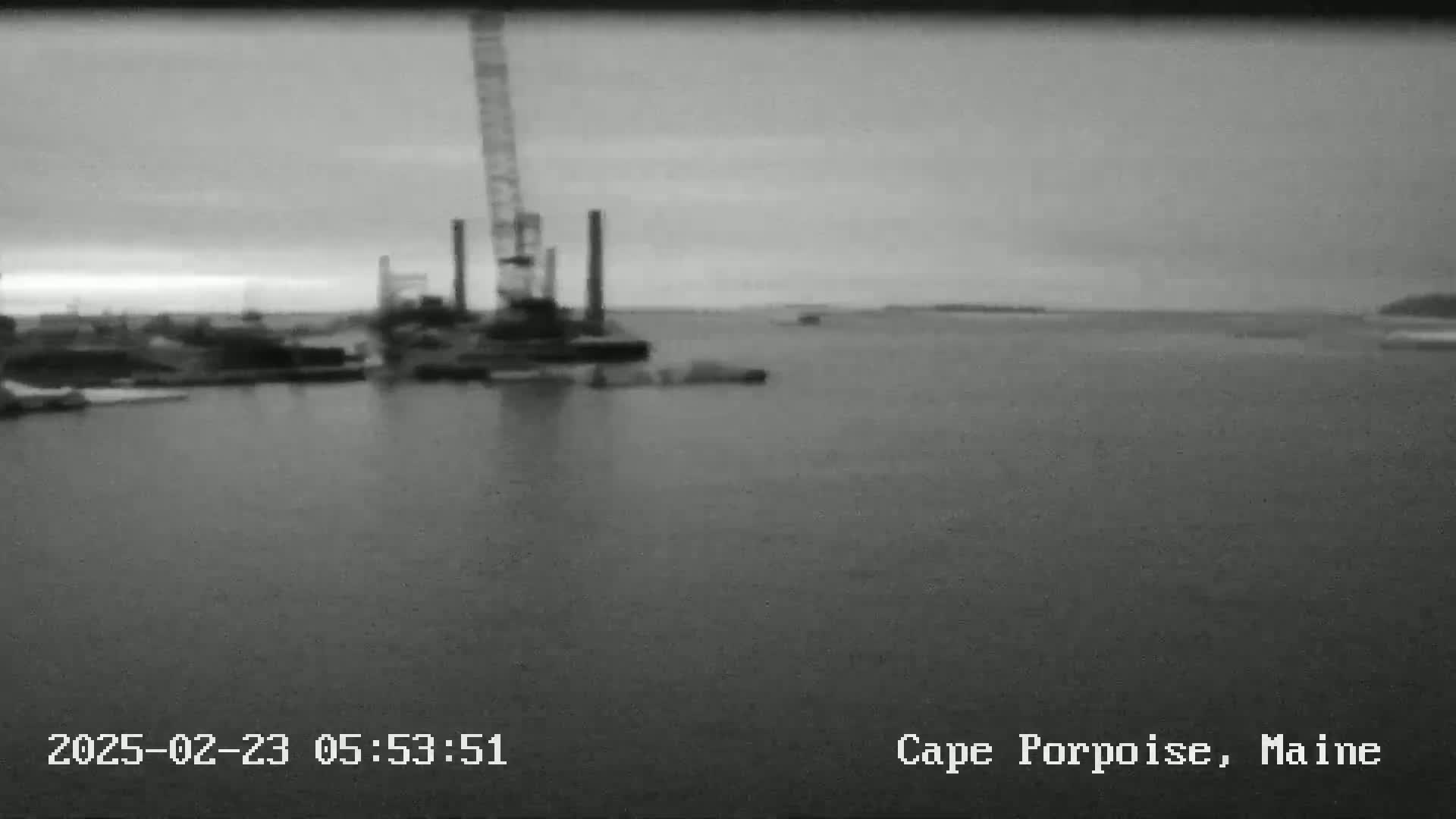 A large crane and other industrial equipment are visible on a body of water under an overcast sky.