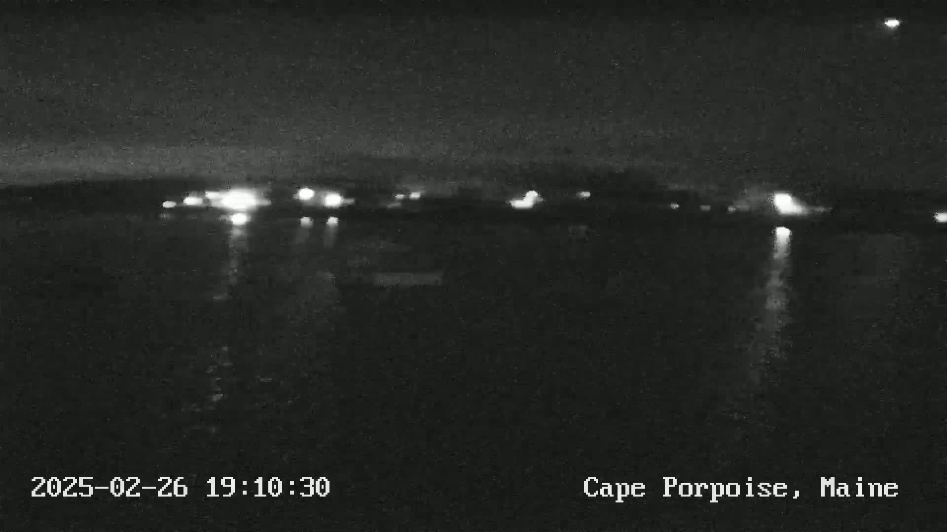 A nighttime, low-light view of a dark body of water reflecting distant lights on a calm surface.