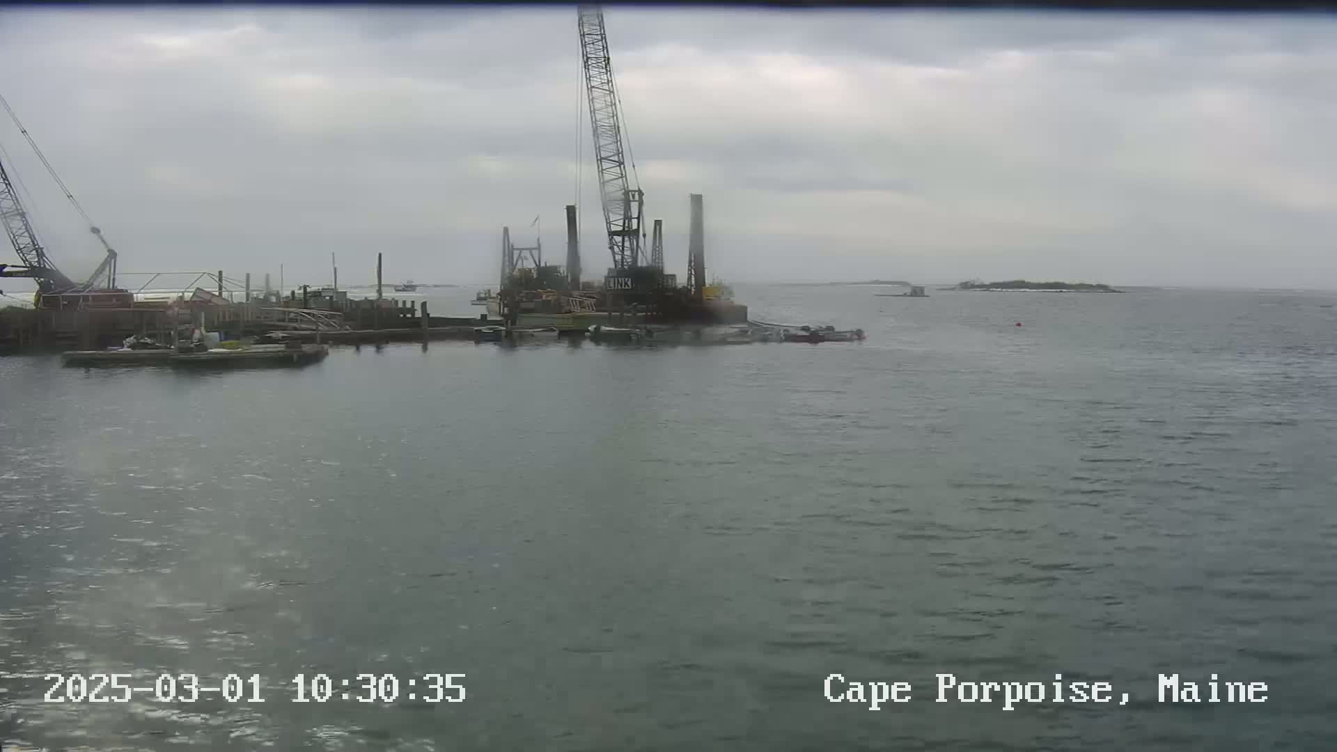 A construction crane and several barges are in a body of water under an overcast sky.