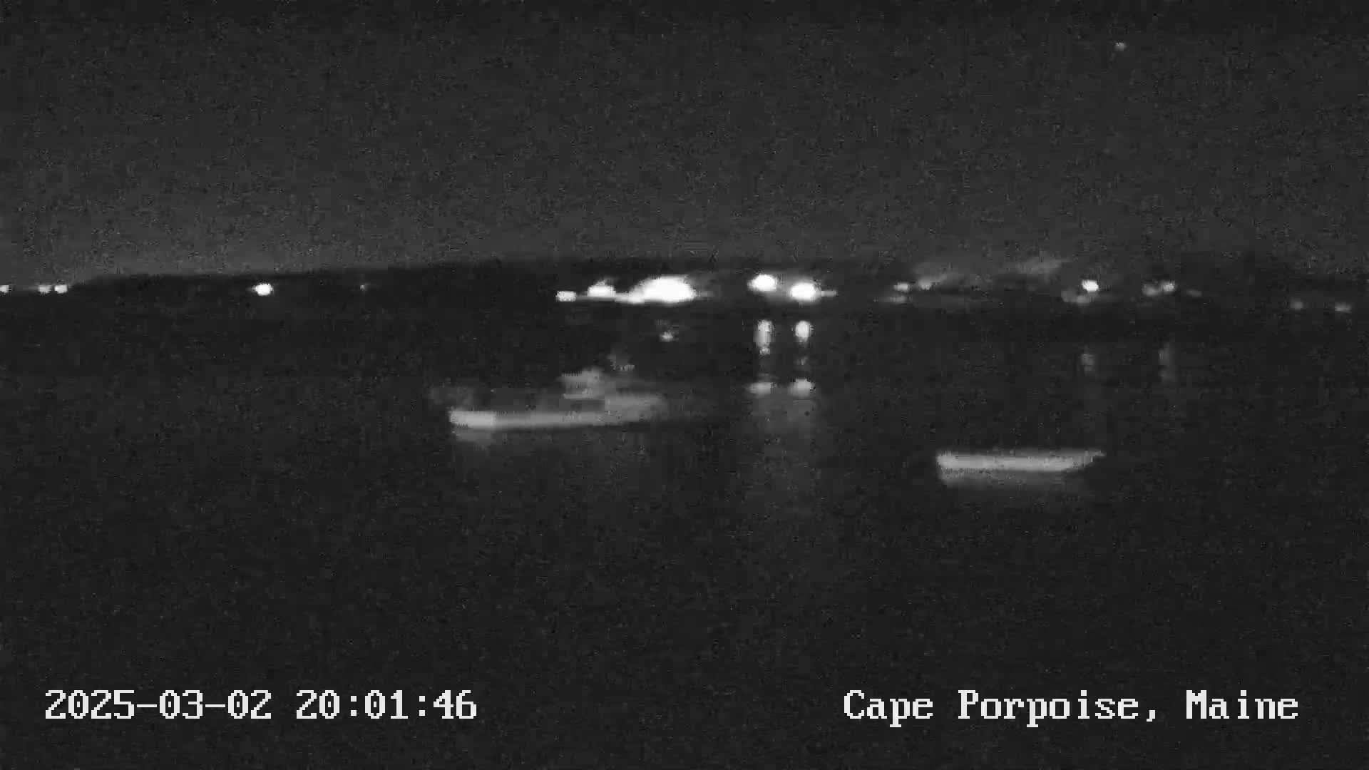 A nighttime, low-light image shows a dark body of water with faint lights on the opposite shore.