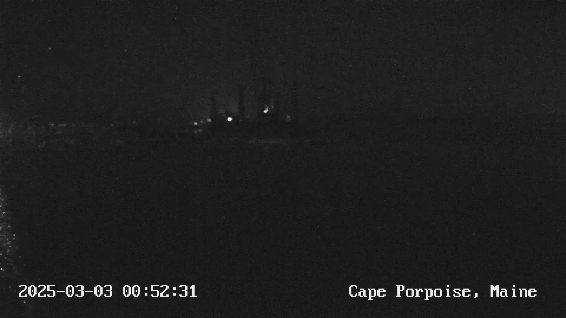 A dark nighttime scene shows a distant cluster of faint lights.