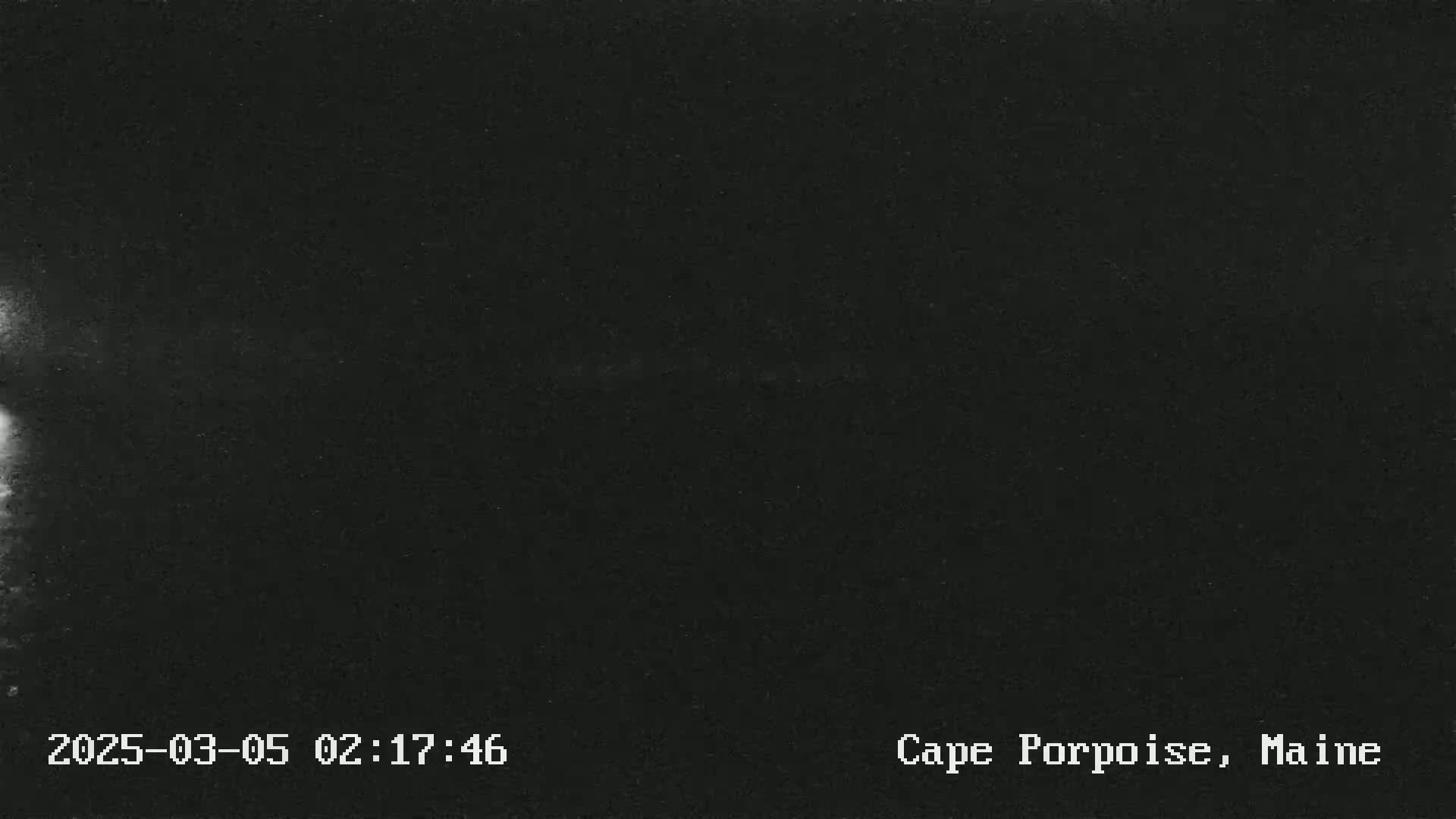 A dark, nighttime outdoor image shows a mostly clear sky with a faint, bright area at the left edge.
