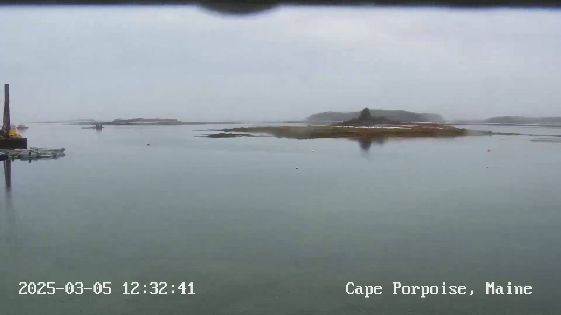 A calm body of water with several small islands and a few boats is seen on an overcast day.