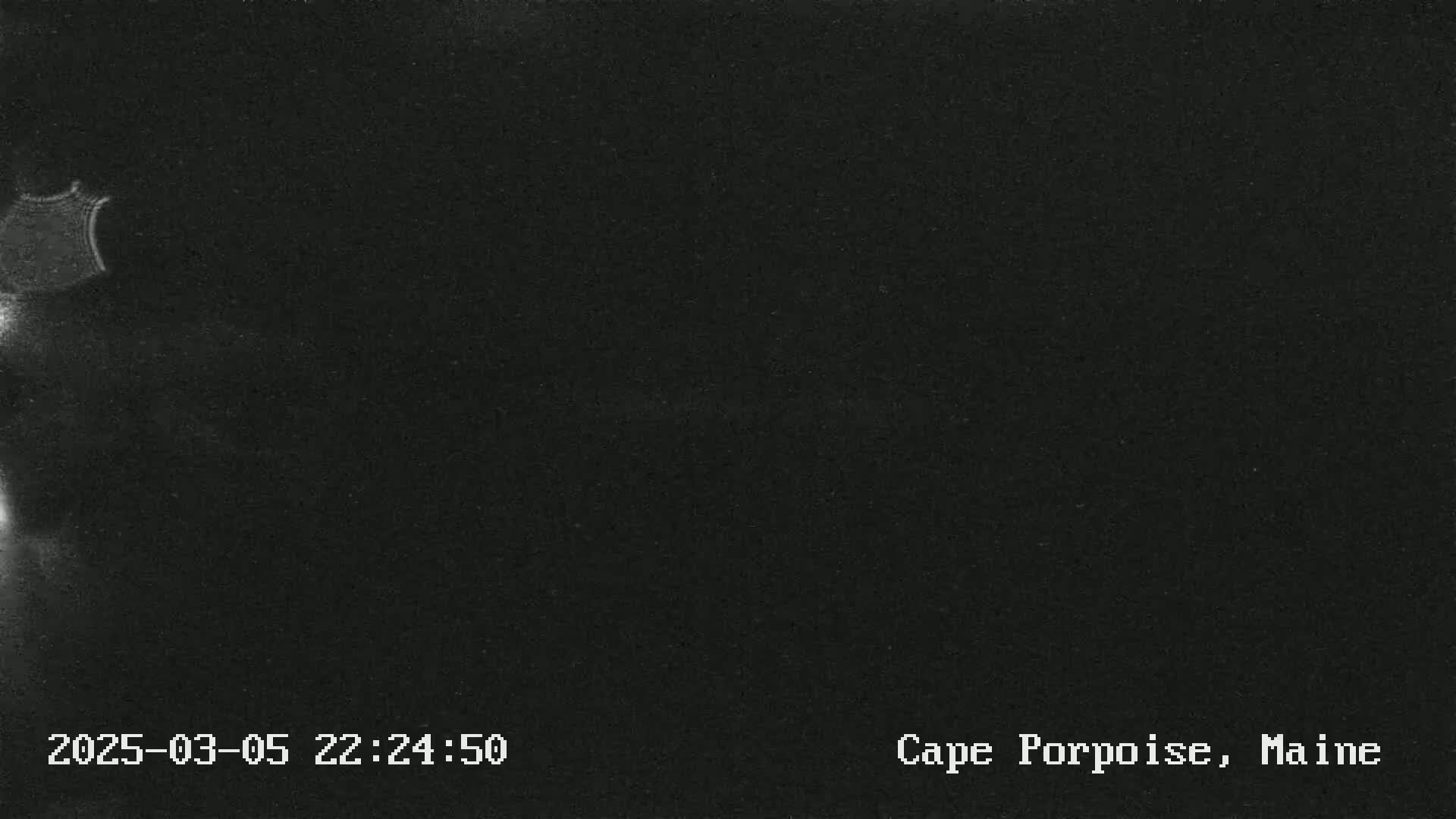 A low-light image shows a dark, possibly nighttime, outdoor scene with a partially visible, indistinct object in the upper left corner.