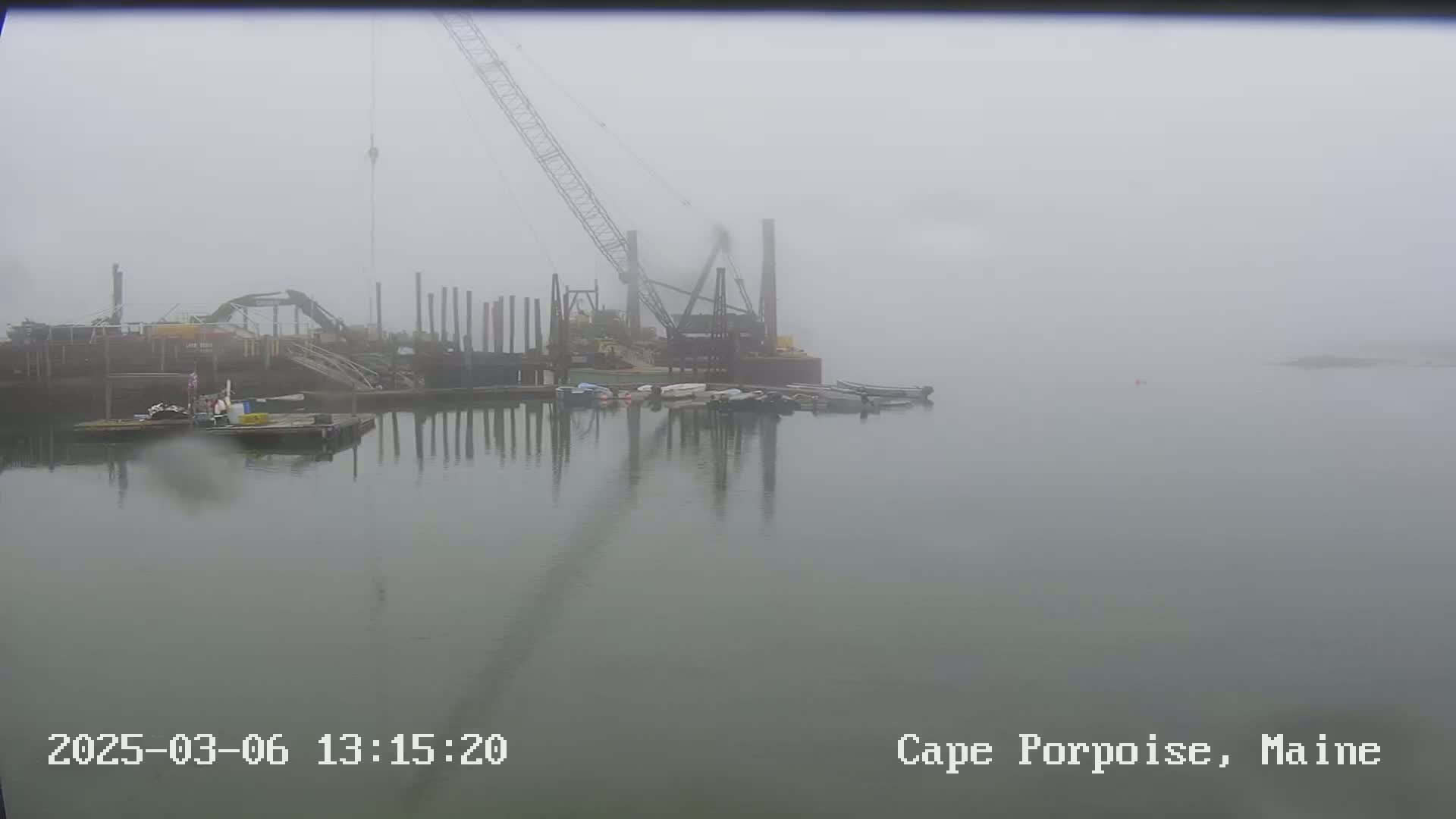 A construction site with a crane and several boats is visible in a foggy harbor.