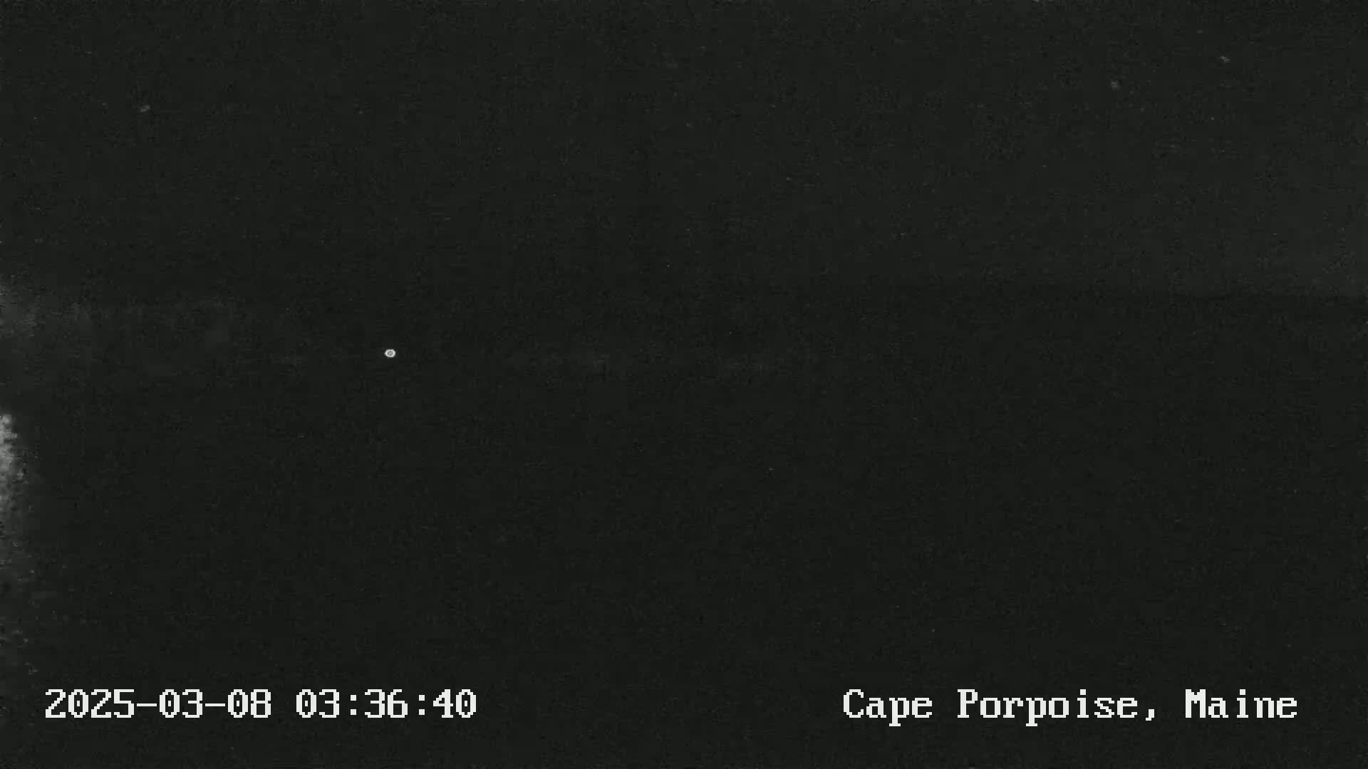 A dark, nighttime image shows a very faint, small light source in the center of the frame against a completely black background.
