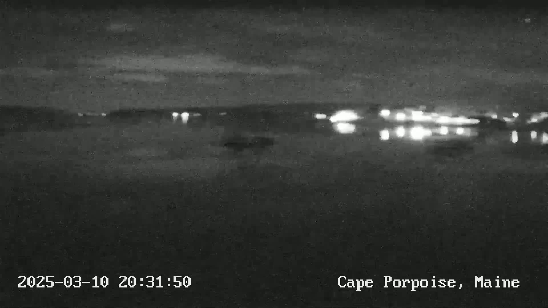 A nighttime, low-light view shows a dark body of water reflecting distant lights.