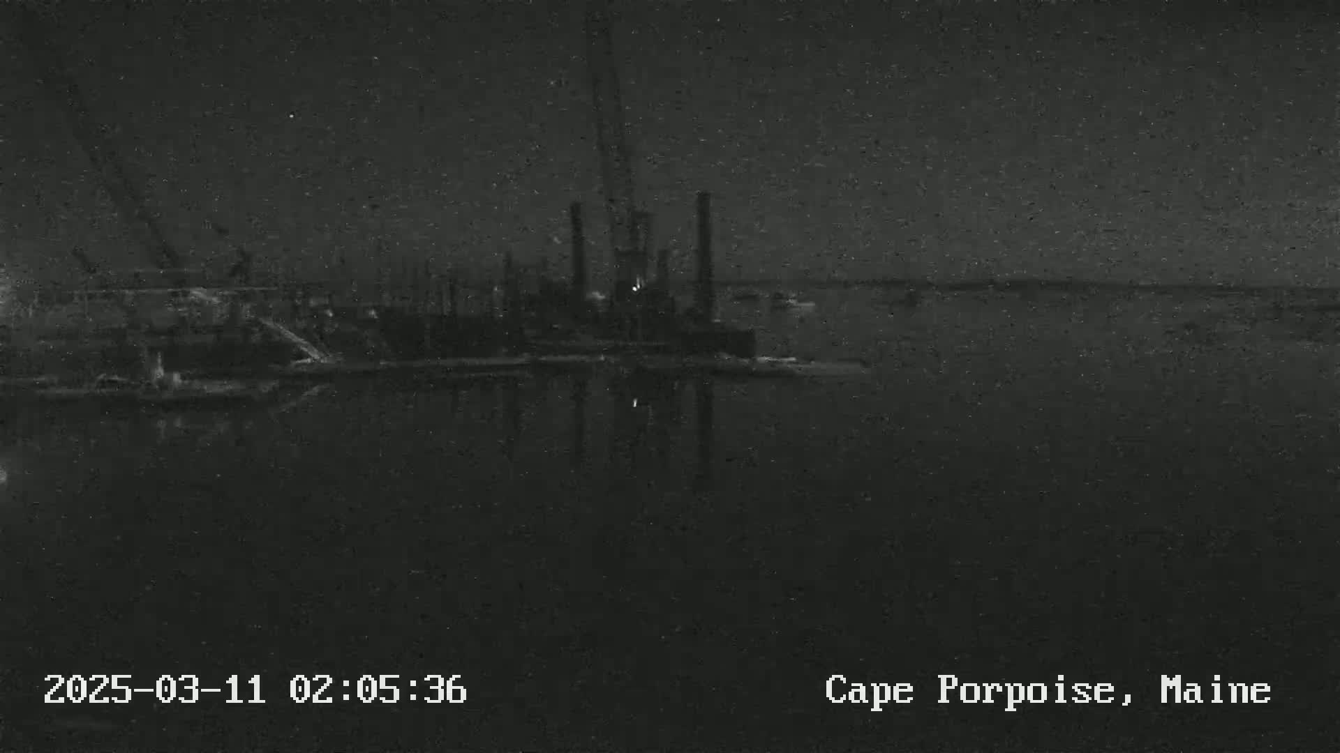 A nighttime, low-light image shows an industrial structure reflected in dark water.