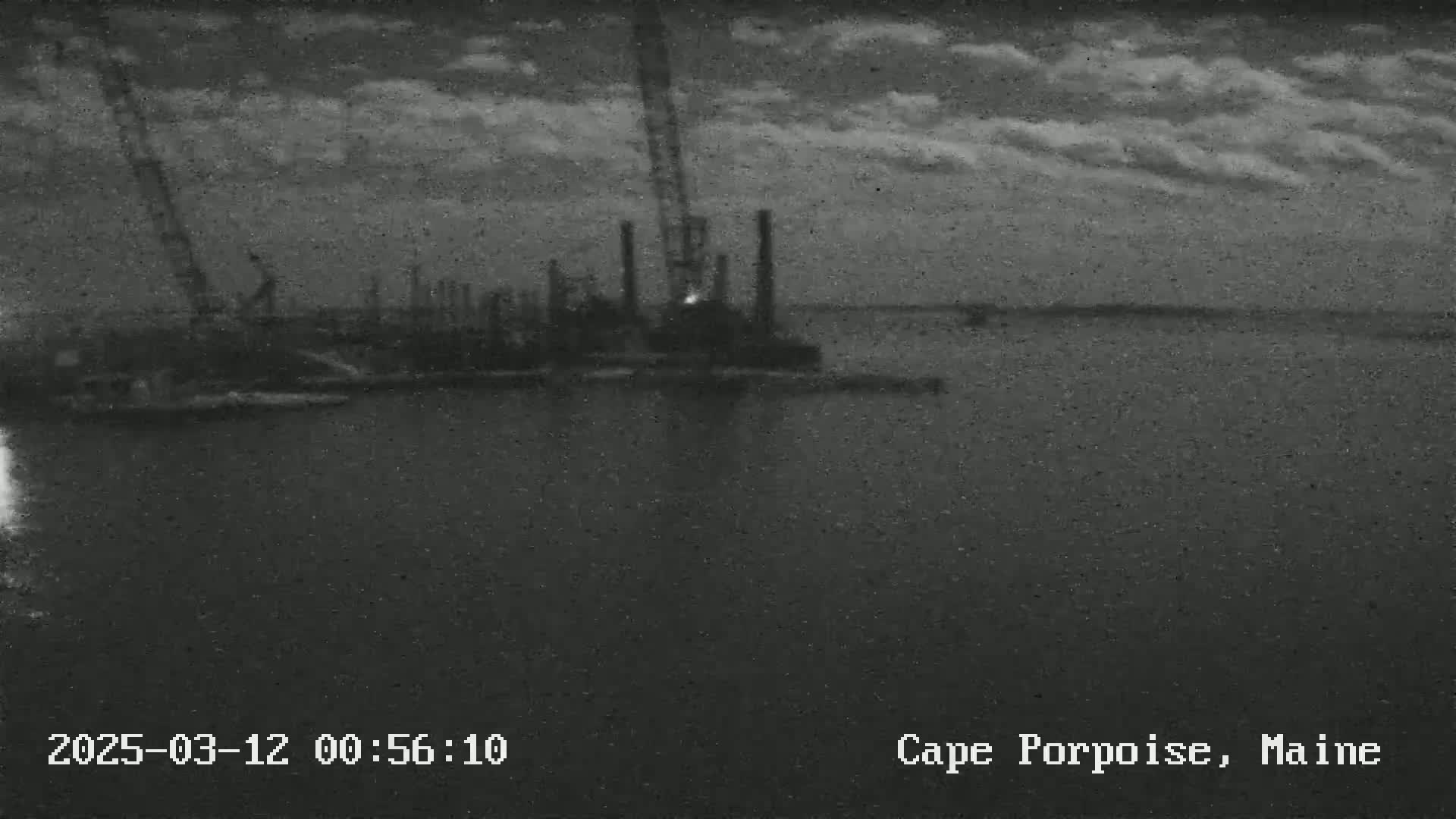 A nighttime, cloudy view of a construction site on the water with several cranes and structures visible.